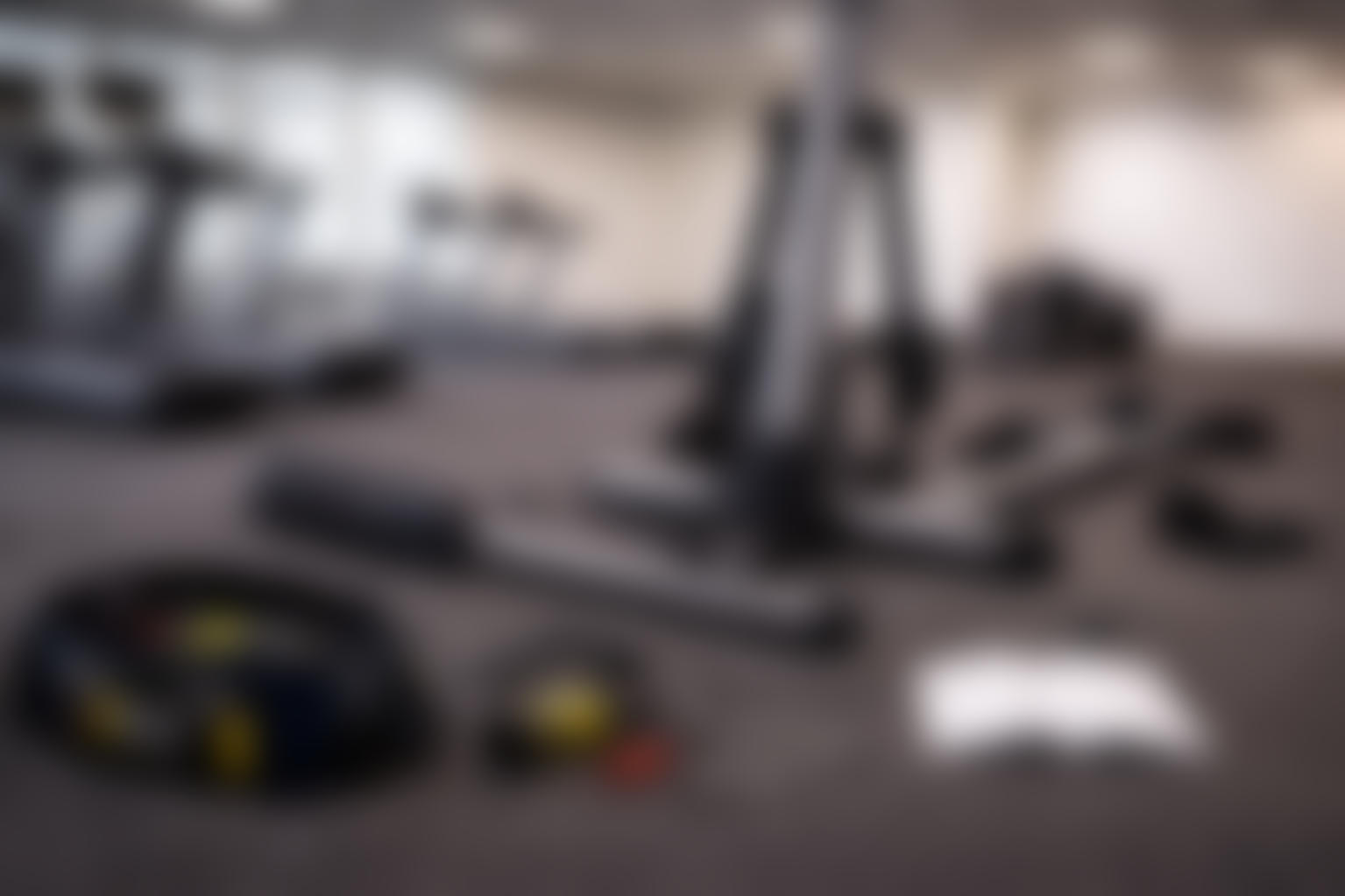 Flat indoor gym with a treadmill, elliptical trainer, and exercise bike, with tools, an open instruction manual, and a tool kit on the floor, indicating equipment assembly or maintenance.