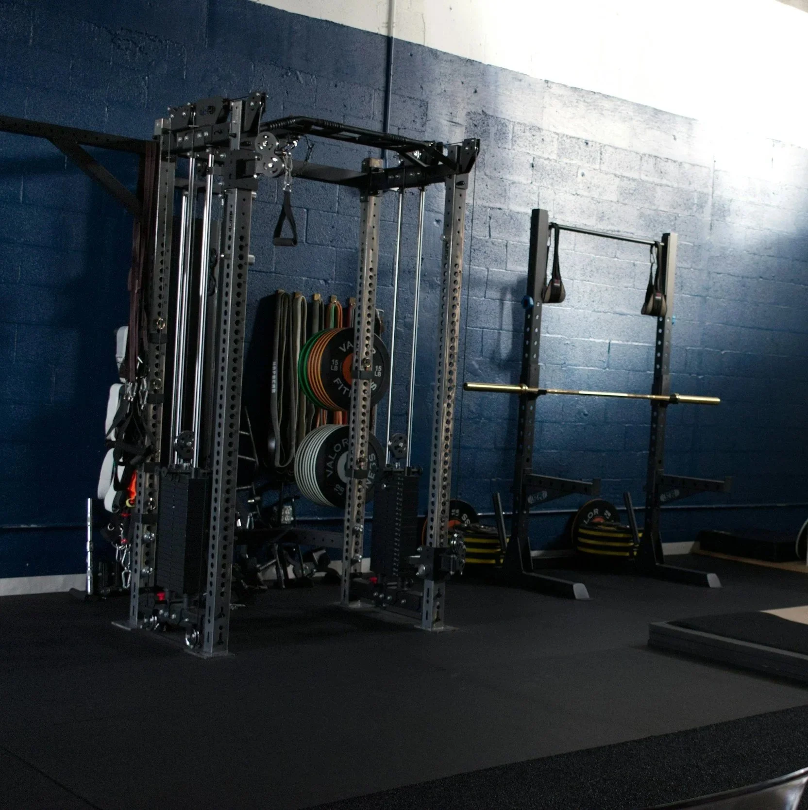 Empty gym with weightlifting equipment, barbells, resistance bands, and weight plates against a blue wall.