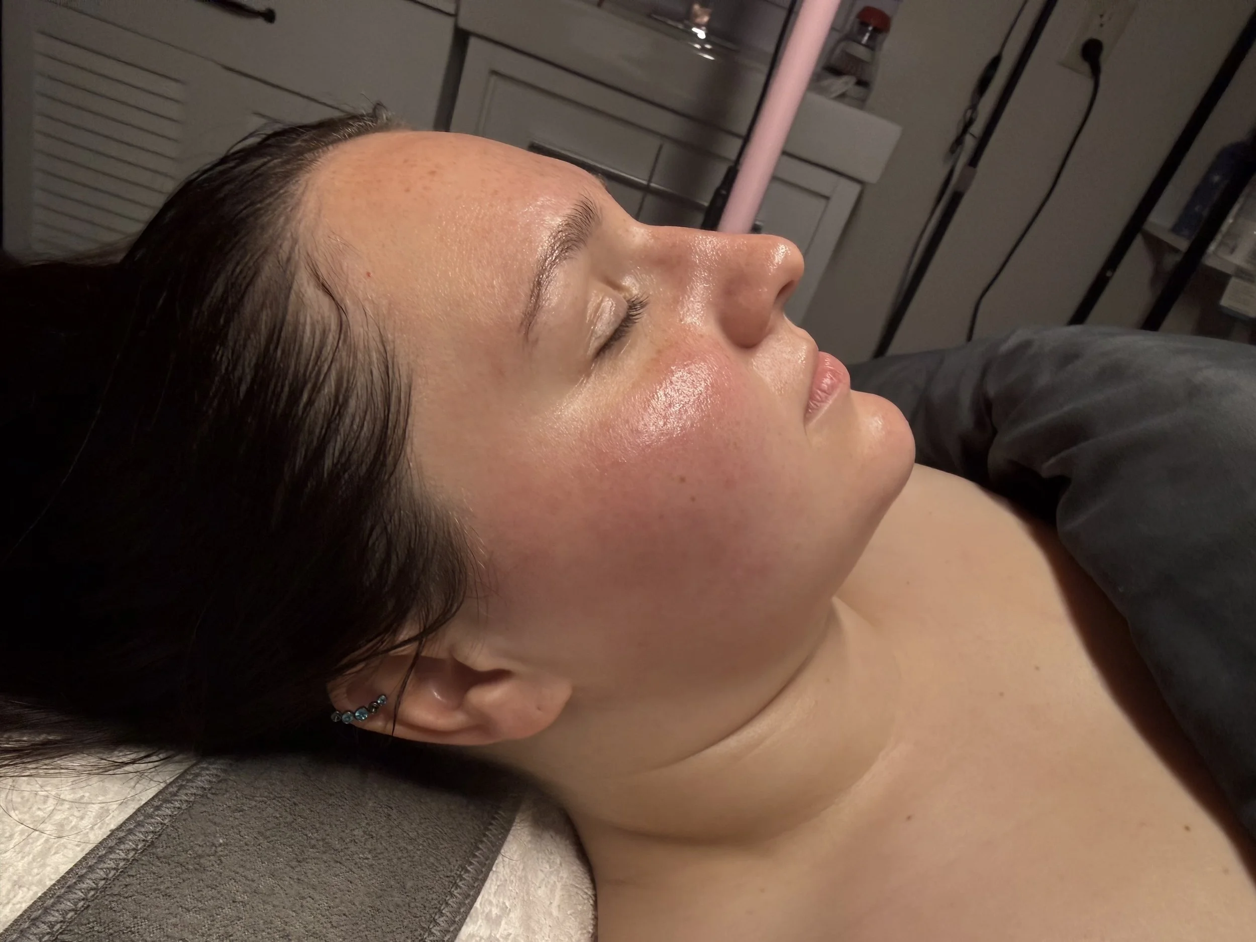 Close-up of a woman with shiny skin, lying down with her eyes closed, in a spa setting after a facial.
