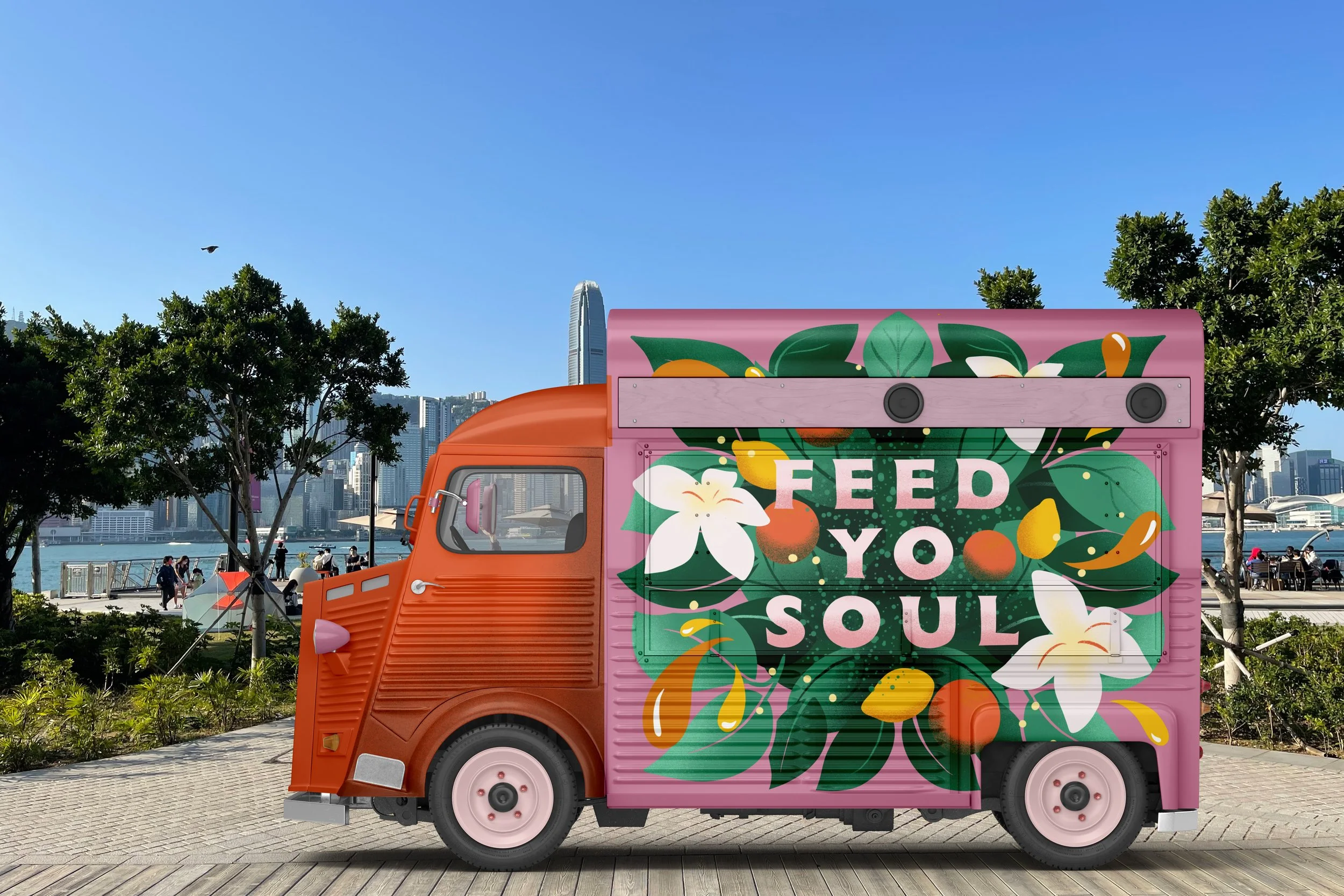 Colorful food truck with pink background and floral design, with the words "Feed Your Soul" in white lettering, parked along a waterfront in a cityscape with trees, skyline, and people in the background.