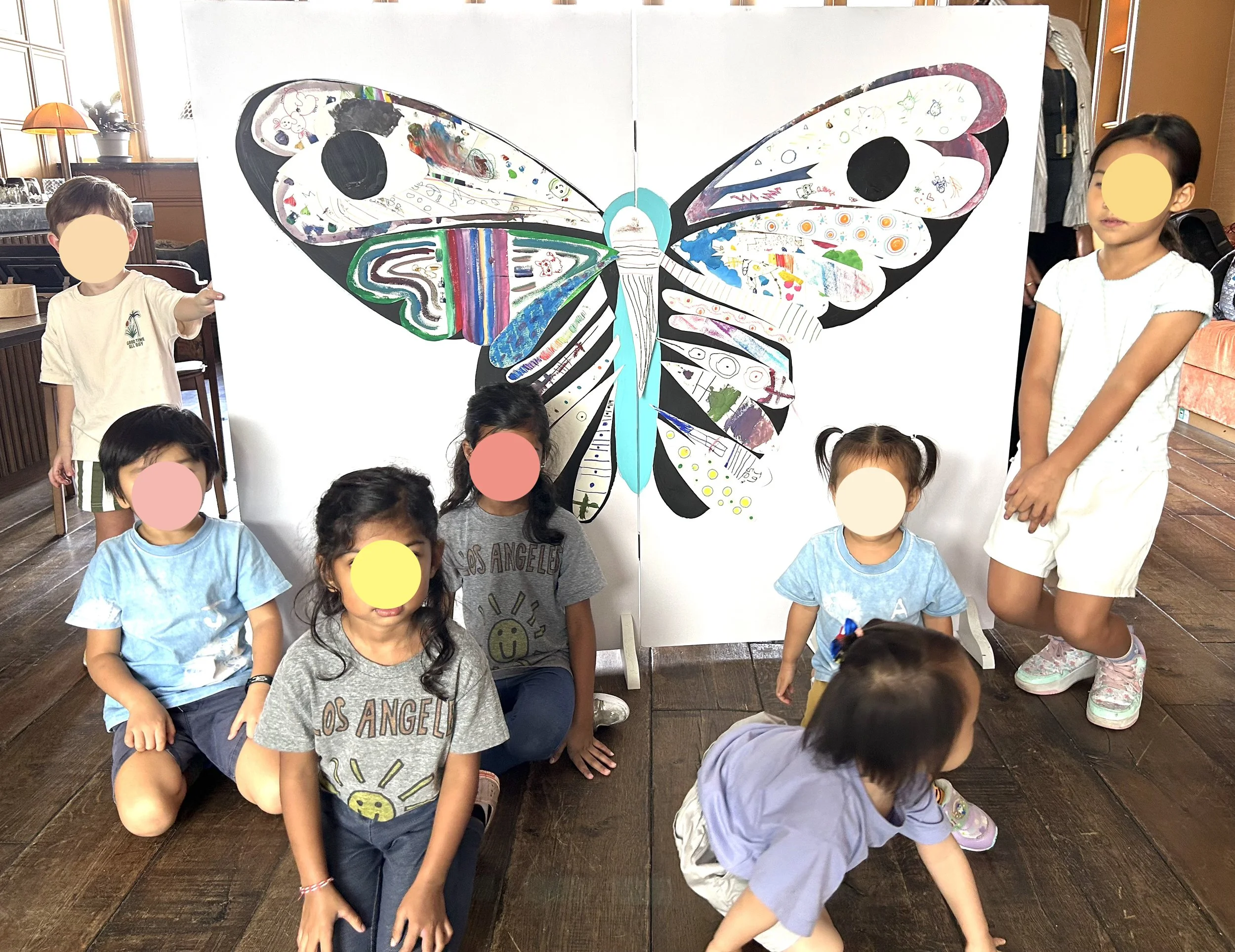 Children posing in front of a large butterfly art display, which is painted with various colorful designs and patterns, in Soho House