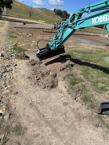 Mini excavator trenching beside a rural driveway in Tasmania