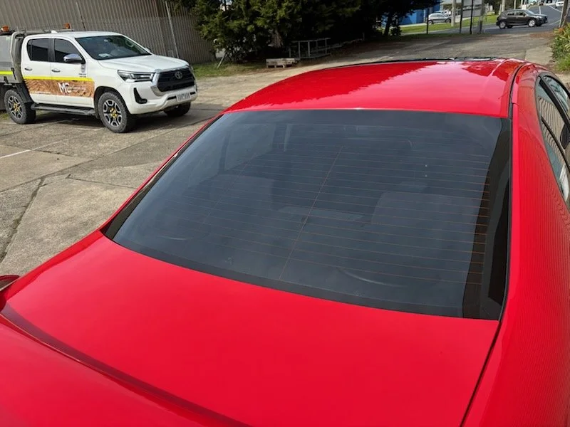 Red car parked in a parking lot with dark rear tinted window