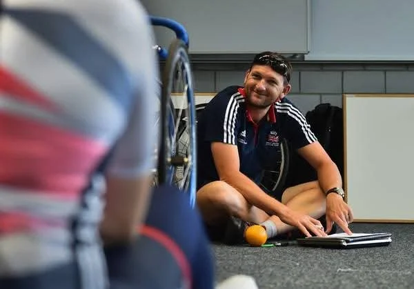 Simon sitting in front of an athlete and pointing to a page.