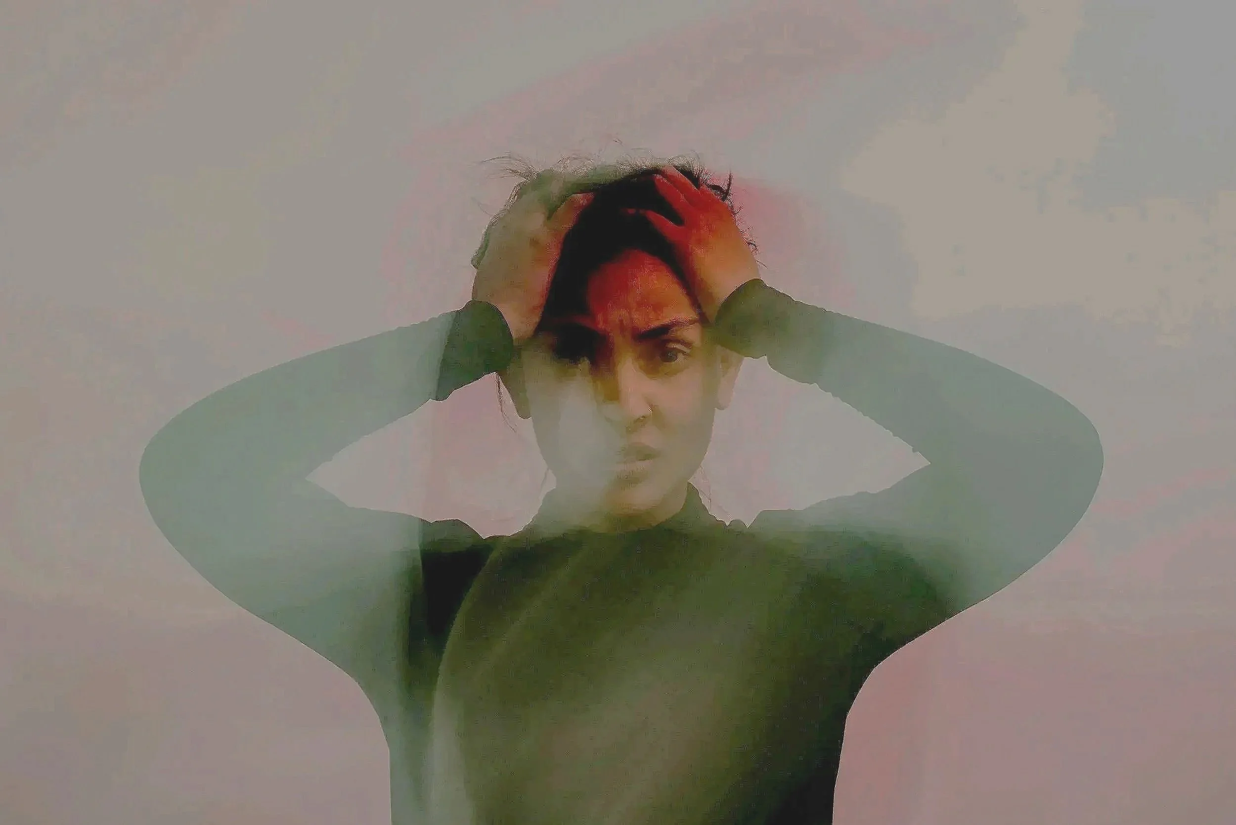 Person with black hair and wearing a dark top holding their head with both hands, looking distressed or worried, against a plain background.