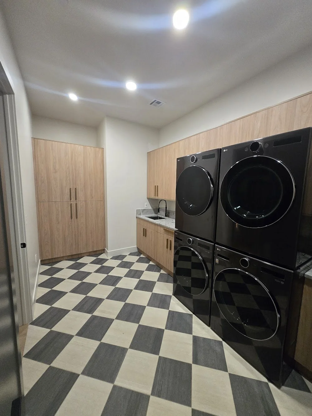 A laundry room with black washer and dryer, wooden cabinets, and a checkered black and beige tile floor.