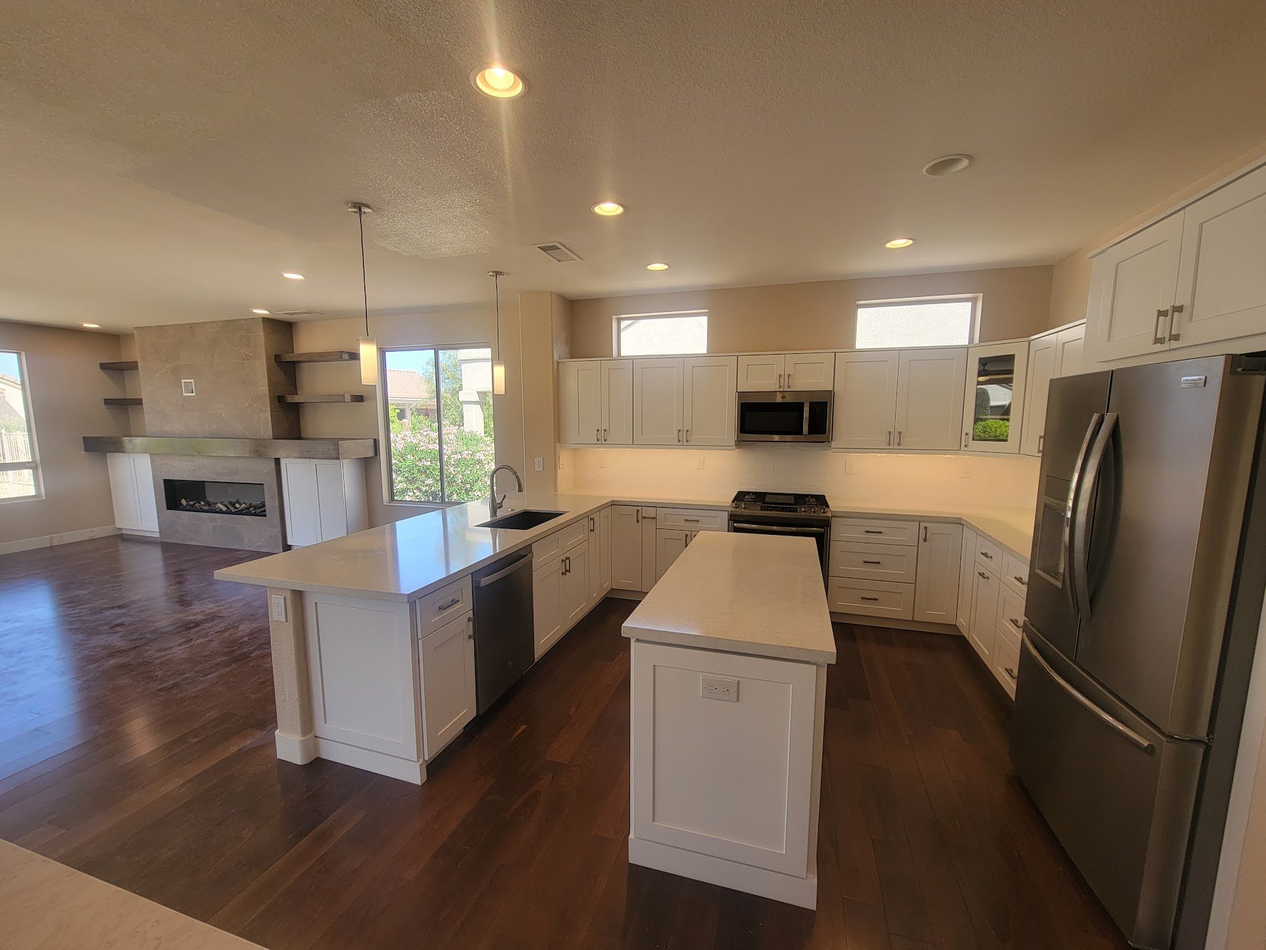 Modern kitchen with white cabinets, stainless steel appliances, central island, dark wooden flooring, and a view of the living area with a fireplace.