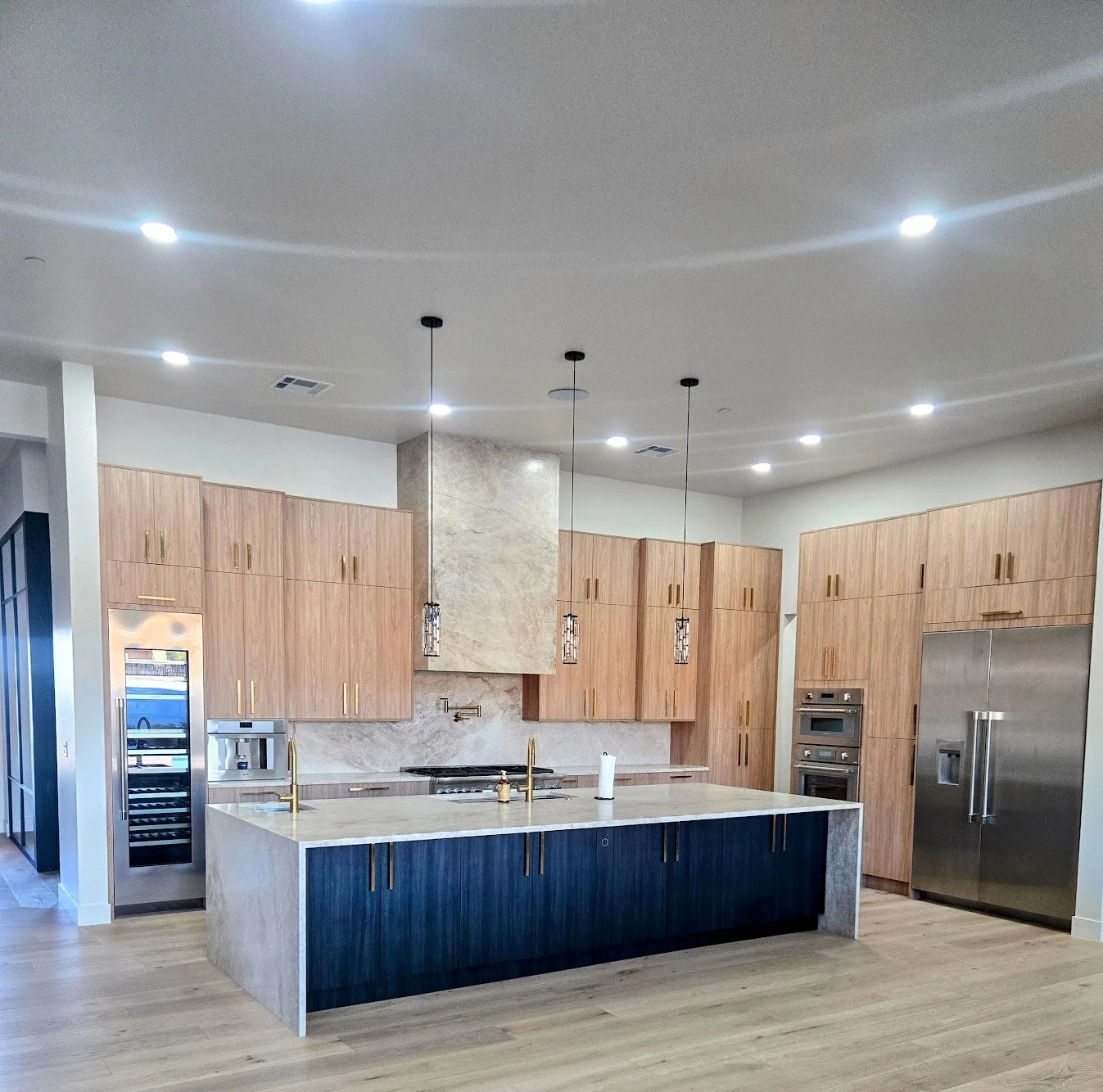 Modern kitchen with a large island, wooden cabinets, stainless steel appliances, and pendant lights.
