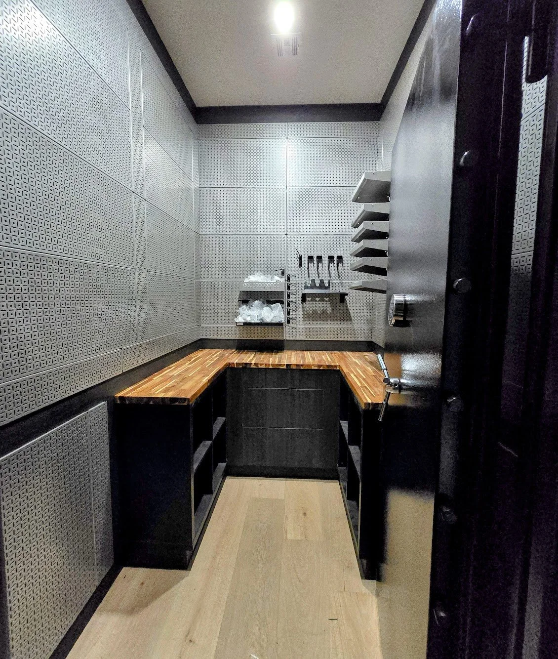 Small room with acoustic panels on the walls, a wooden counter, and wall-mounted shelves holding knives and plastic bags.