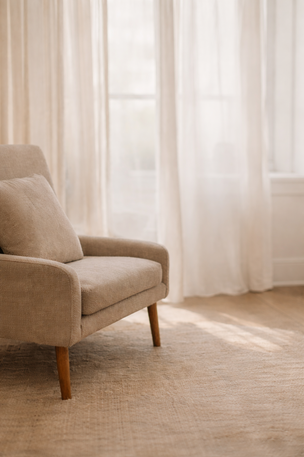 A beige armchair with wooden legs in a sunlit room with white curtains."}how to style it? When determining how to style a room containing this armchair, consider the aesthetic you want to achieve. For a cozy, minimalistic look, keep decorations simple with neutral tones and soft textiles. Add a small side table and a throw blanket for warmth. For a more vibrant style, incorporate colorful pillows, artwork, and patterned rugs to create visual interest. Layer different textures to enhance depth, such as a plush rug, woven baskets, or textured cushions. Keep the space uncluttered for a clean look or add decorative accessories for personality. Use warm lighting to complement the neutral palette and create a welcoming atmosphere.
