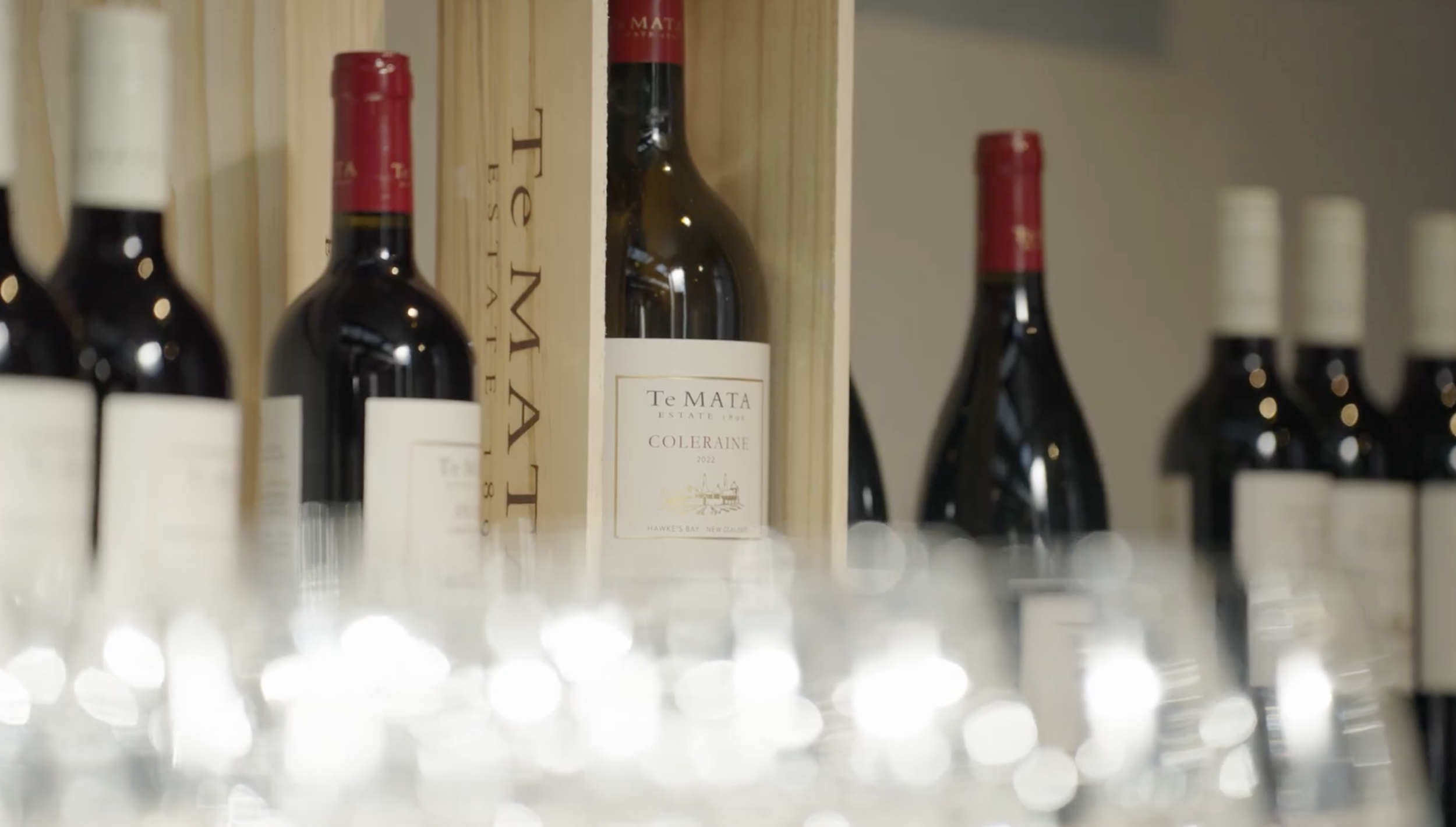 Product photography of  'Te Mata Estate Coleraine 2022' in a wooden crate, and a blurred row of glasses in the foreground.
