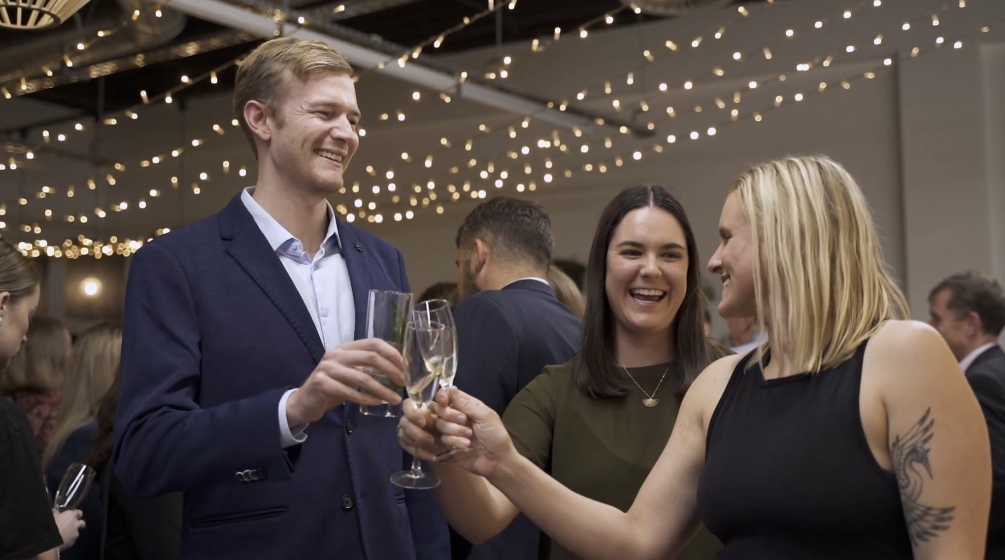 People celebrating at a party with string lights overhead, holding champagne glasses.