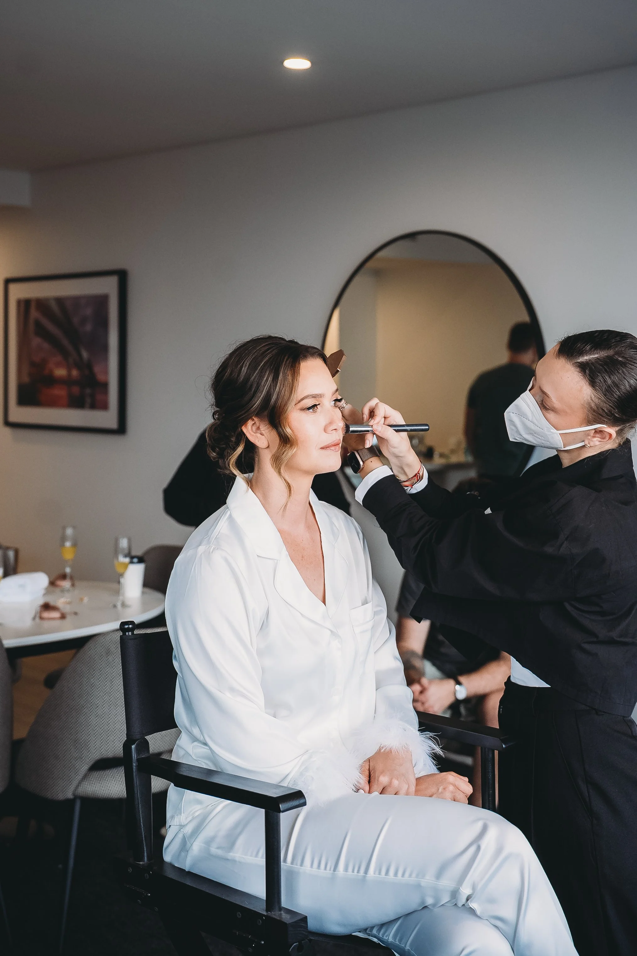 Makeup artist applying makeup to a model sitting in a salon or studio setting.