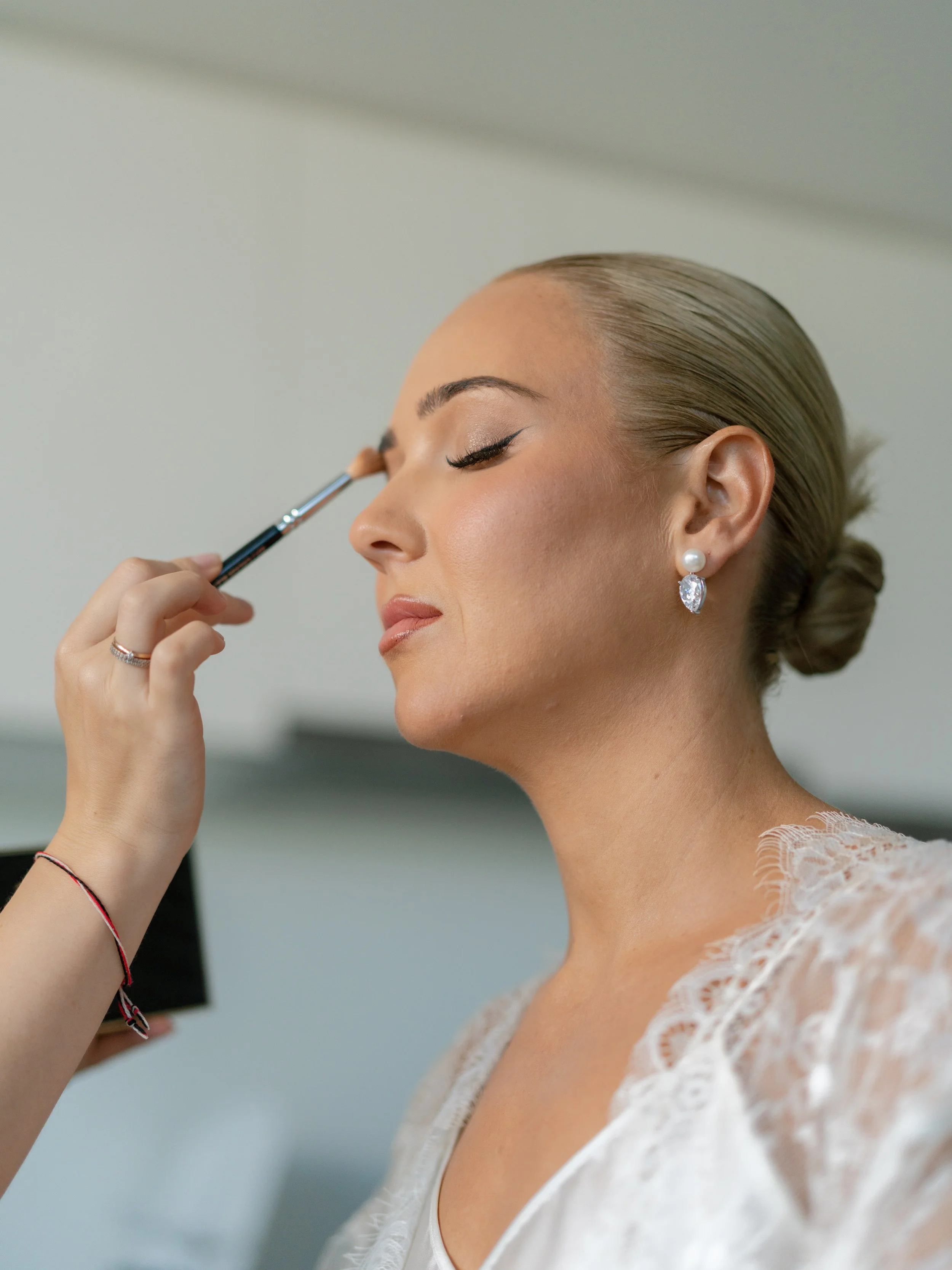 A woman with her eyes closed as a makeup artist applies eyeshadow with a brush.