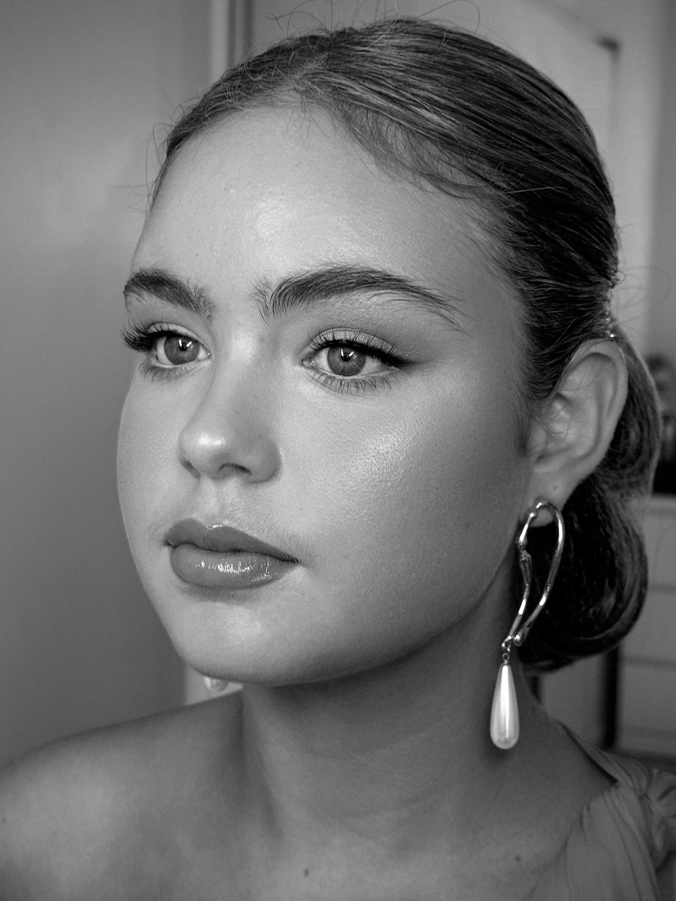 Black and white close-up portrait of a young woman with her hair styled in an elegant updo, wearing a dangling earring with a pearl pendant, and looking slightly to the side.