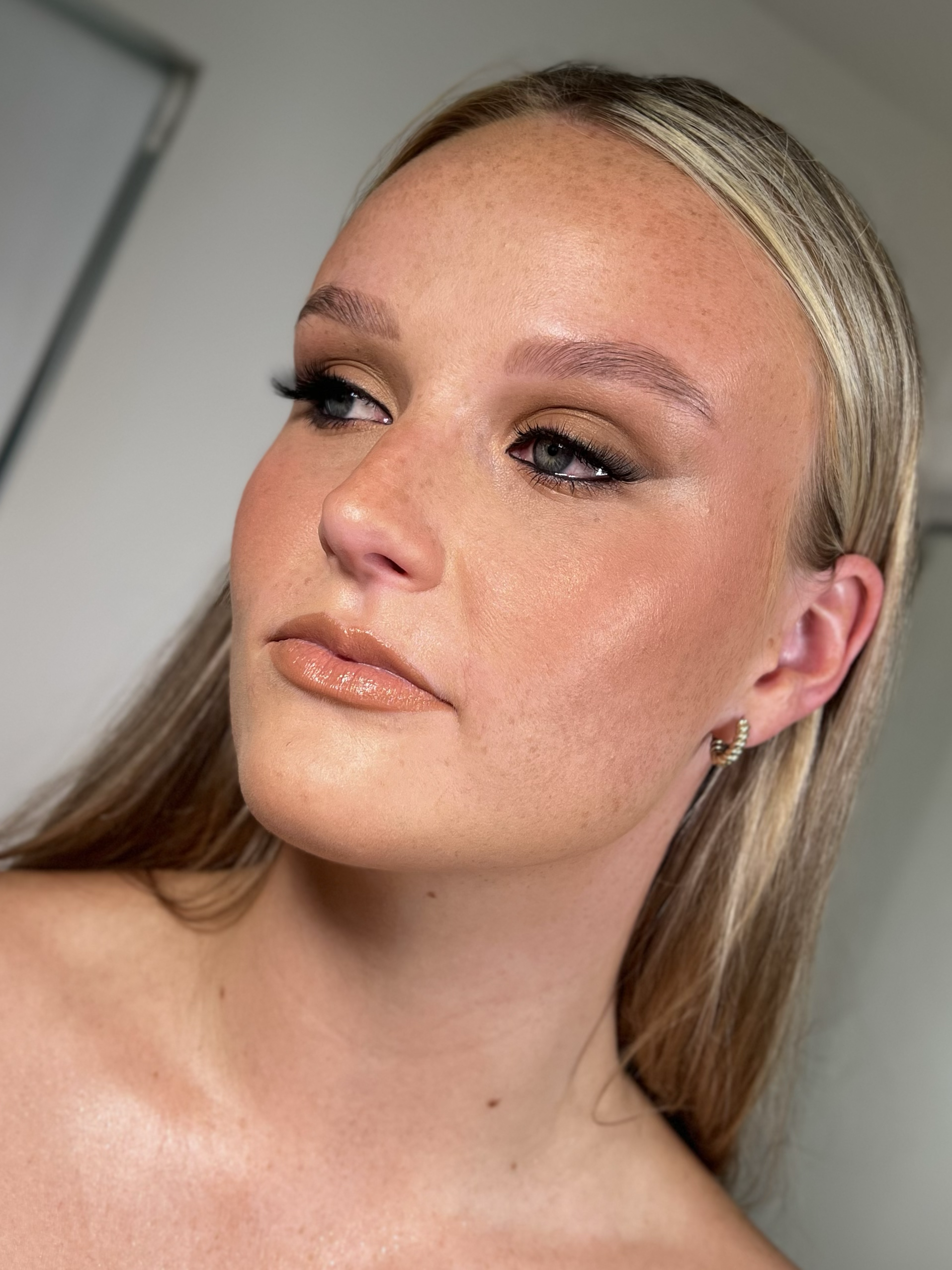 Close-up of a woman with makeup, including nude lipstick, eye makeup, and earrings, looking slightly to the side.