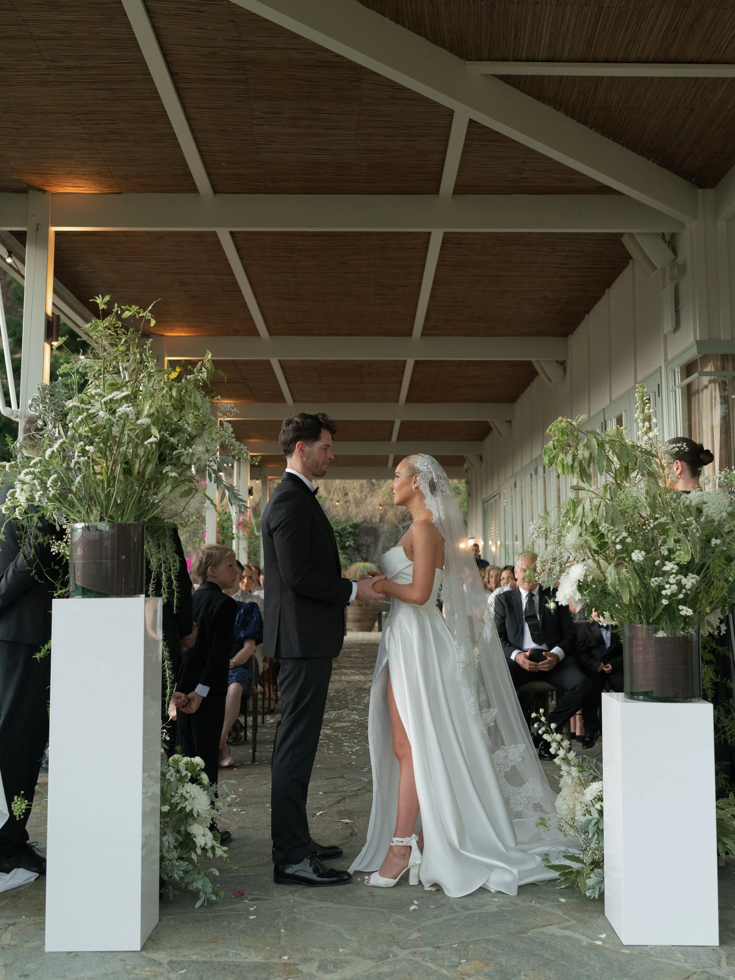 A bride and groom holding hands during their wedding ceremony in a decorated outdoor venue.