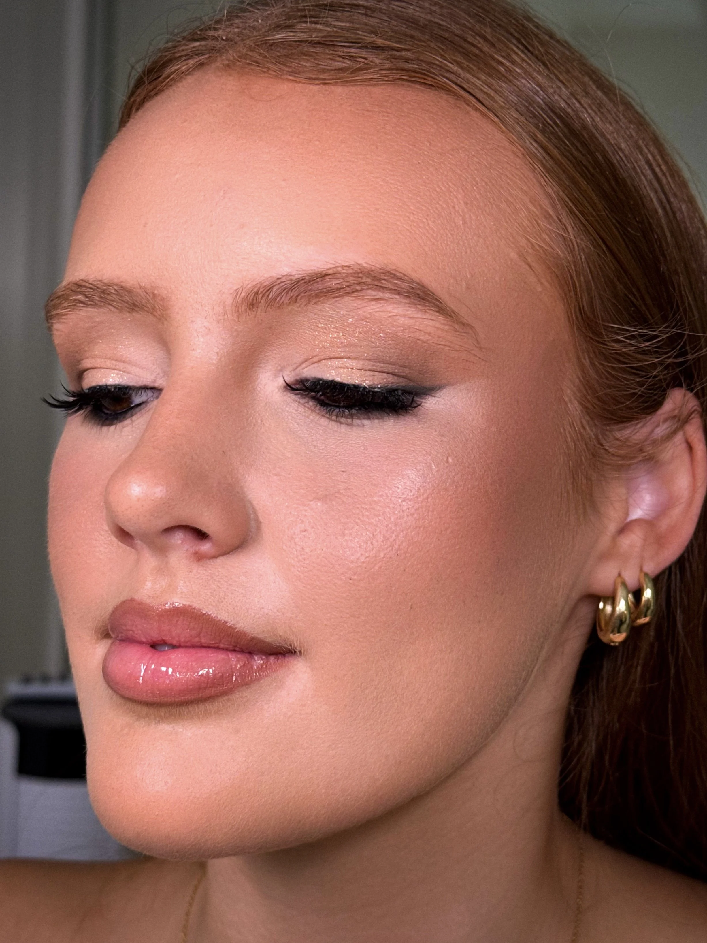 Close-up of a woman's face with makeup, gold earrings, and red hair, with her eyes closed.