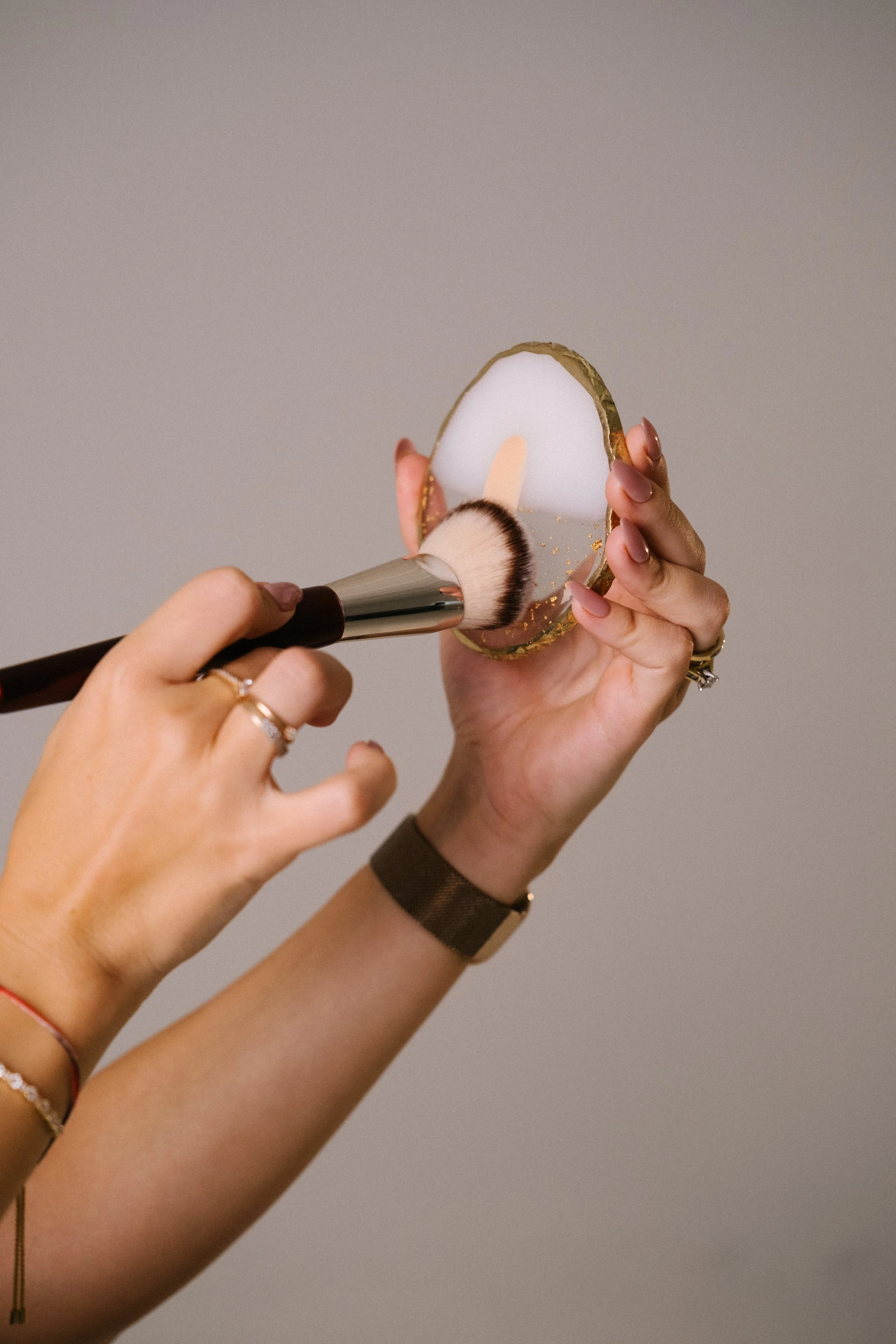 Person holding a decorative mirror and applying makeup with a brush.