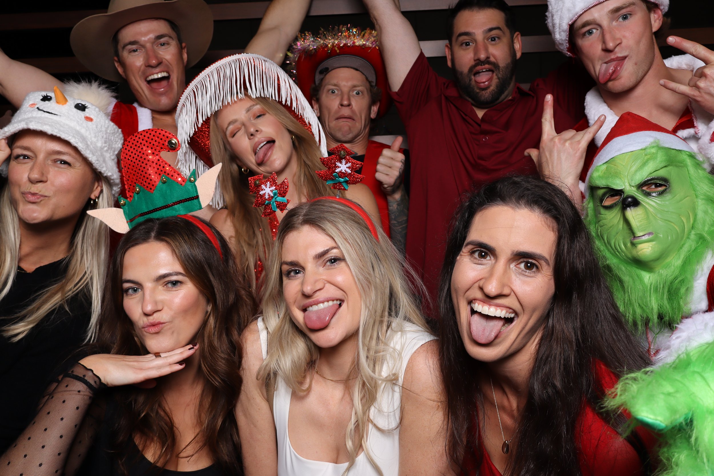 Group of people at a festive holiday party, wearing Christmas accessories and costumes, making silly faces, and celebrating.