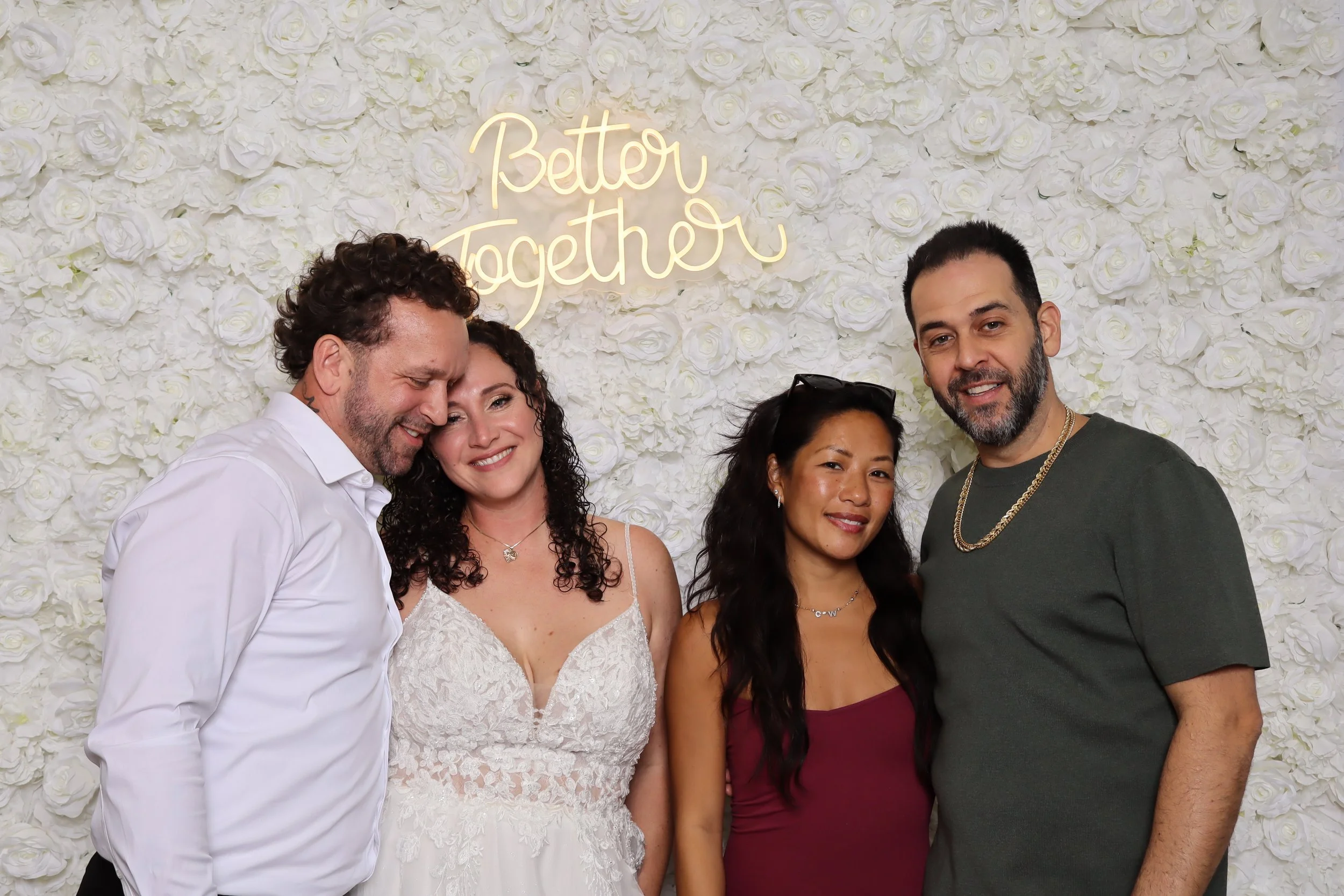 Four people standing in front of a white floral wall with a neon sign that reads "Better Together."