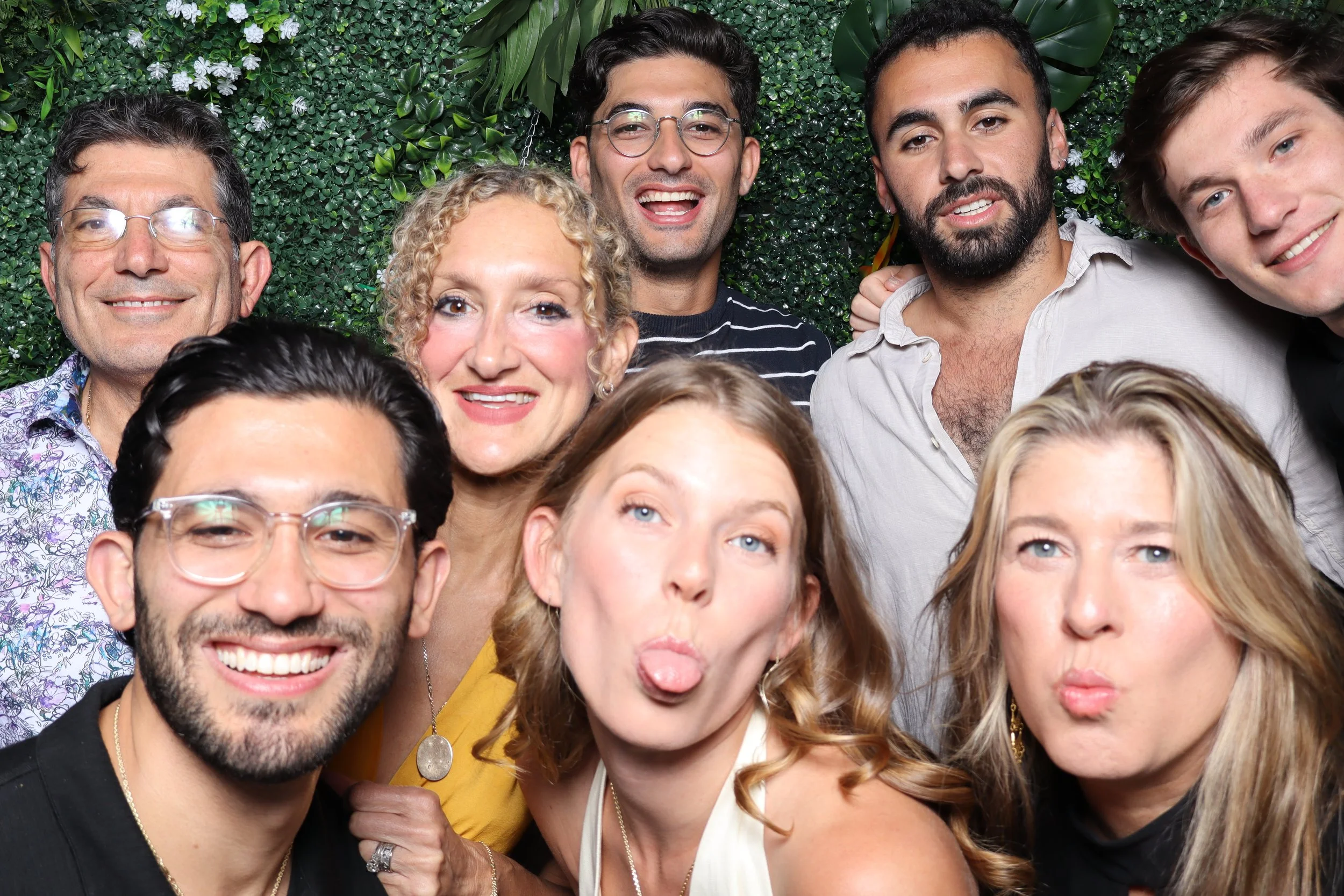 Group of nine diverse friends smiling and making faces for a photo against a green leafy backdrop.