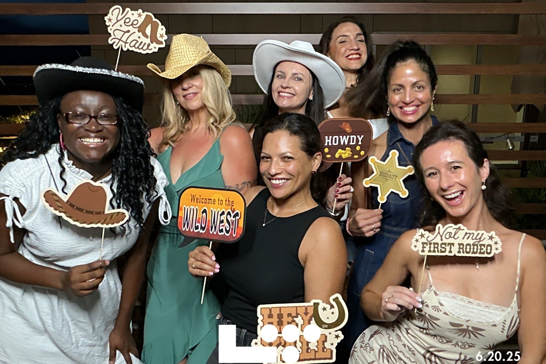 Group of women dressed in Western-themed attire with cowboy hats and props, smiling at a party or celebration.