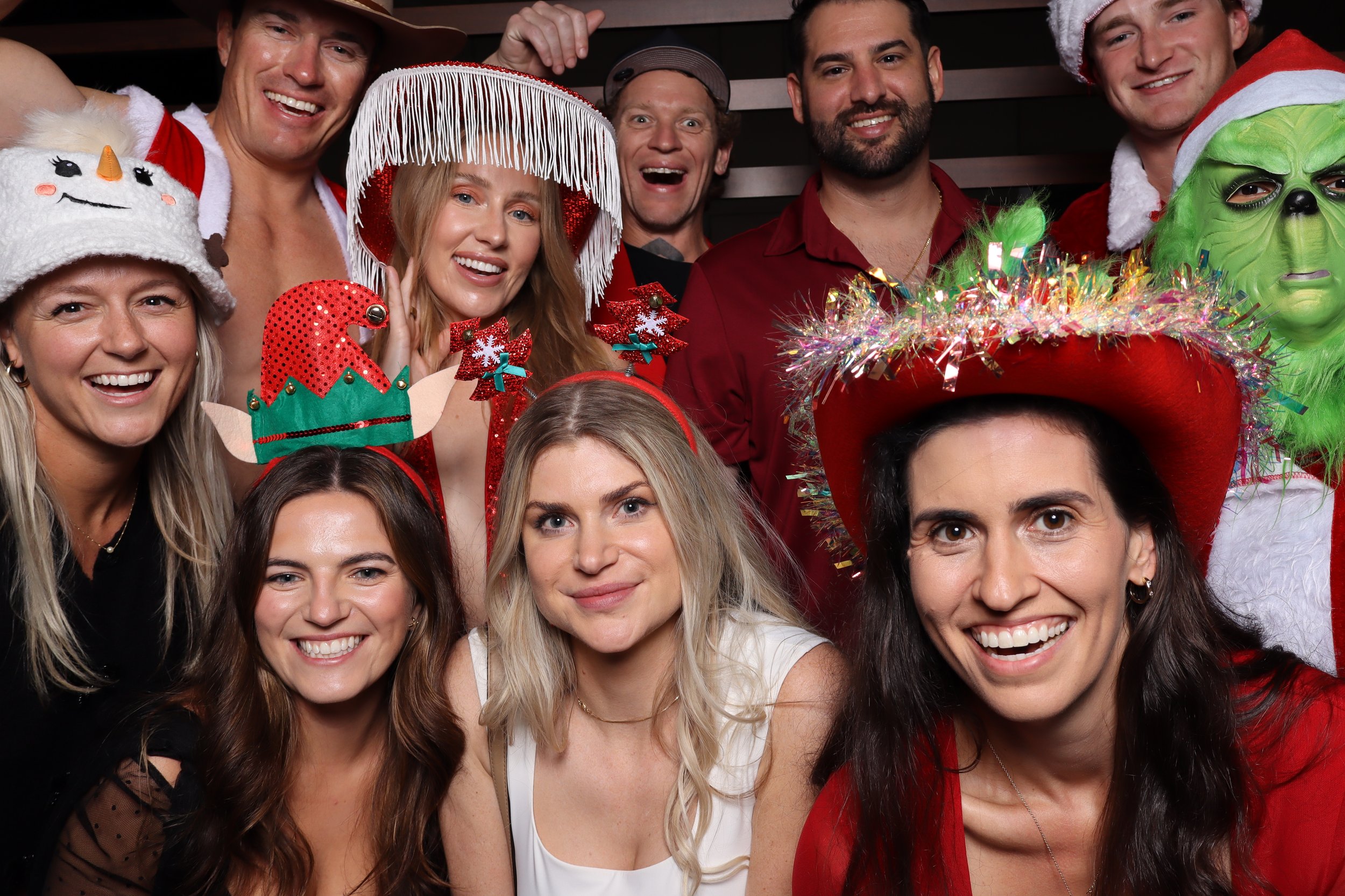 Group of people wearing Christmas-themed hats and accessories, smiling for a photo at a holiday celebration.