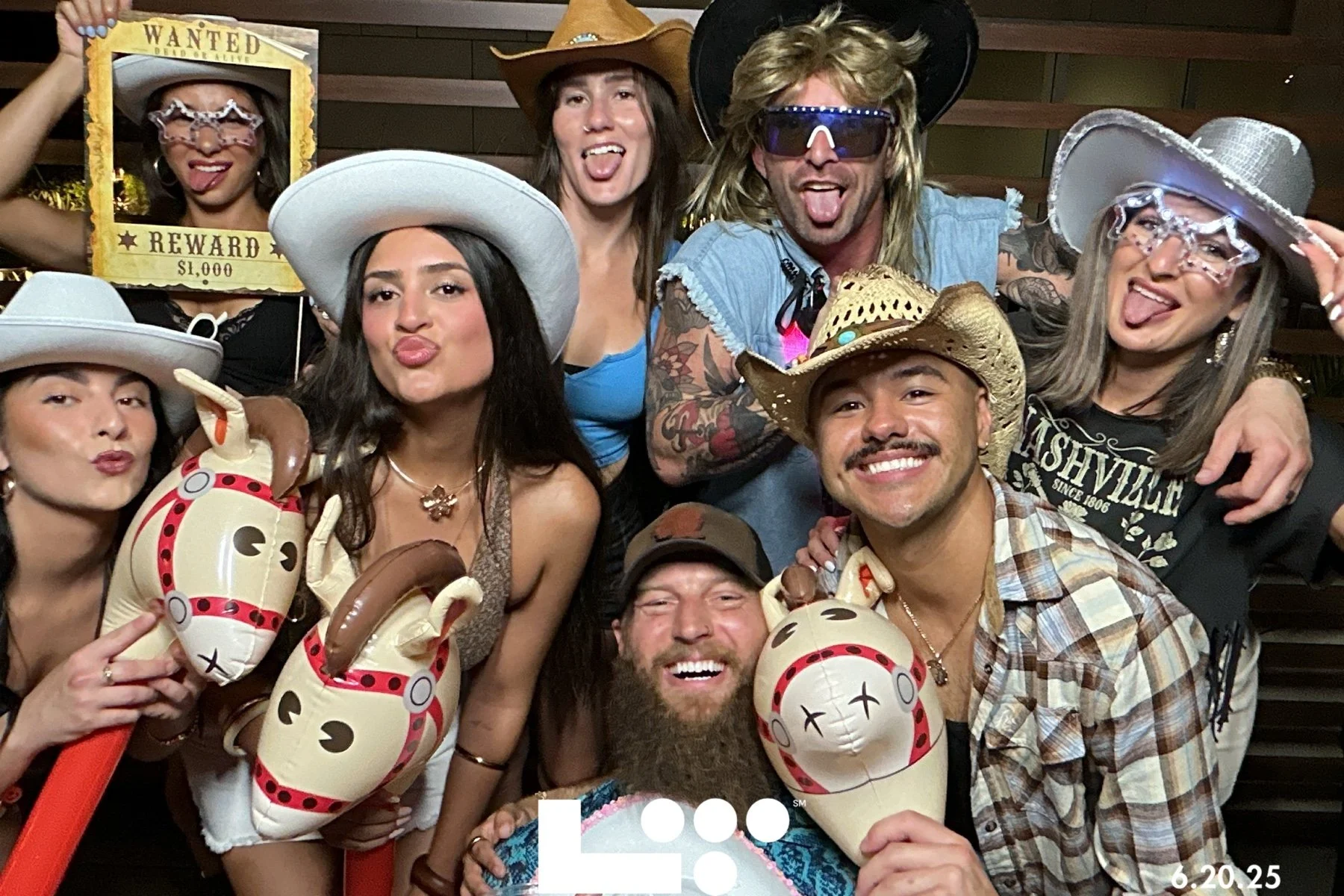 A group of people dressed in cowboy and Western-themed costumes, including hats, sunglasses, and balloons, celebrating and posing cheerfully for the camera.