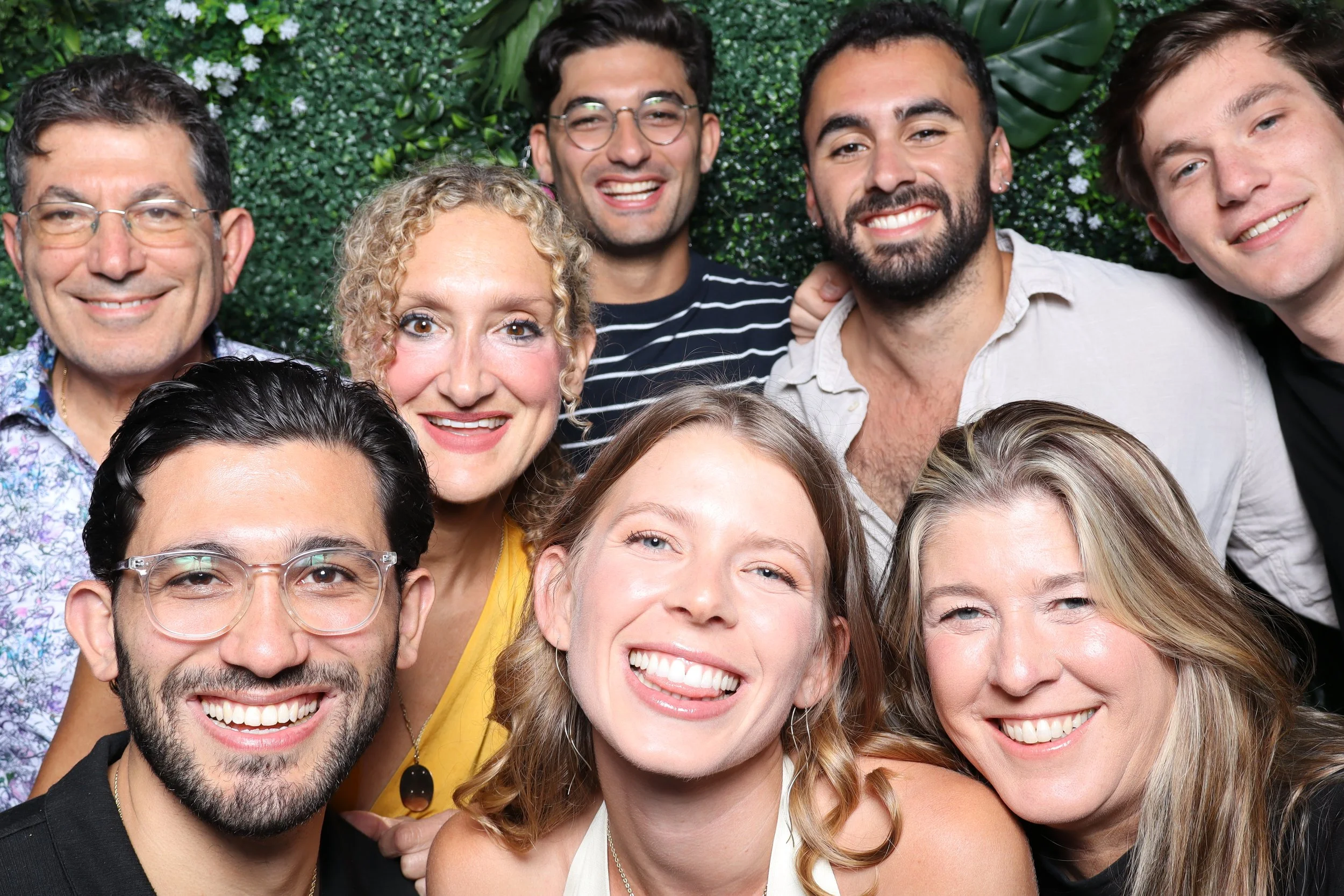 Group of smiling diverse friends posing together in front of a green leafy background.