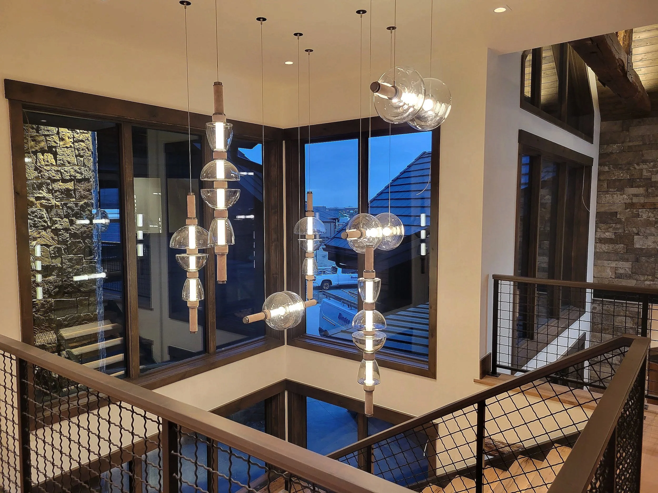 Interior view of a modern upstairs area with a hanging light fixture and large windows showing the exterior of neighboring houses at dusk.