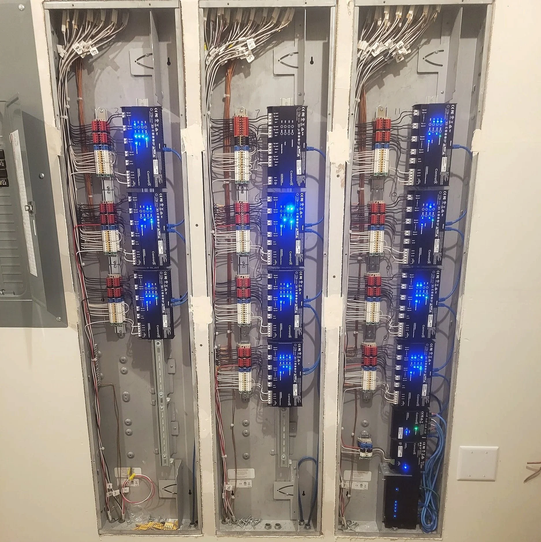 Electrical control panels with blue LED displays and wiring inside a wall.