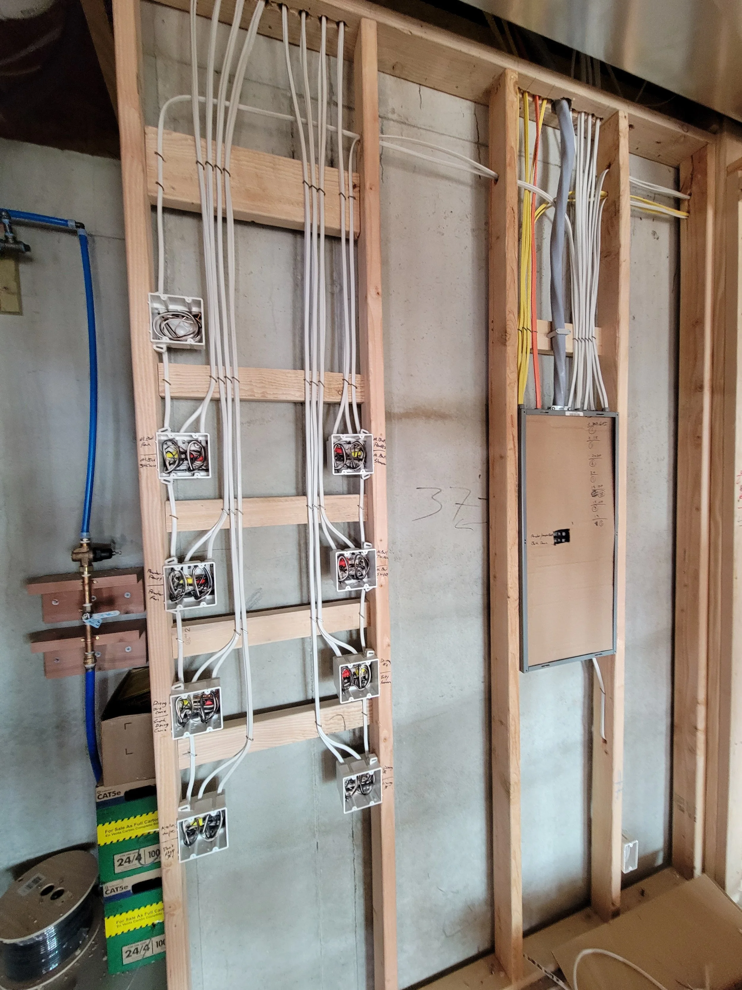 Electrical wiring and panels installed on a wooden wall framework in a construction site.