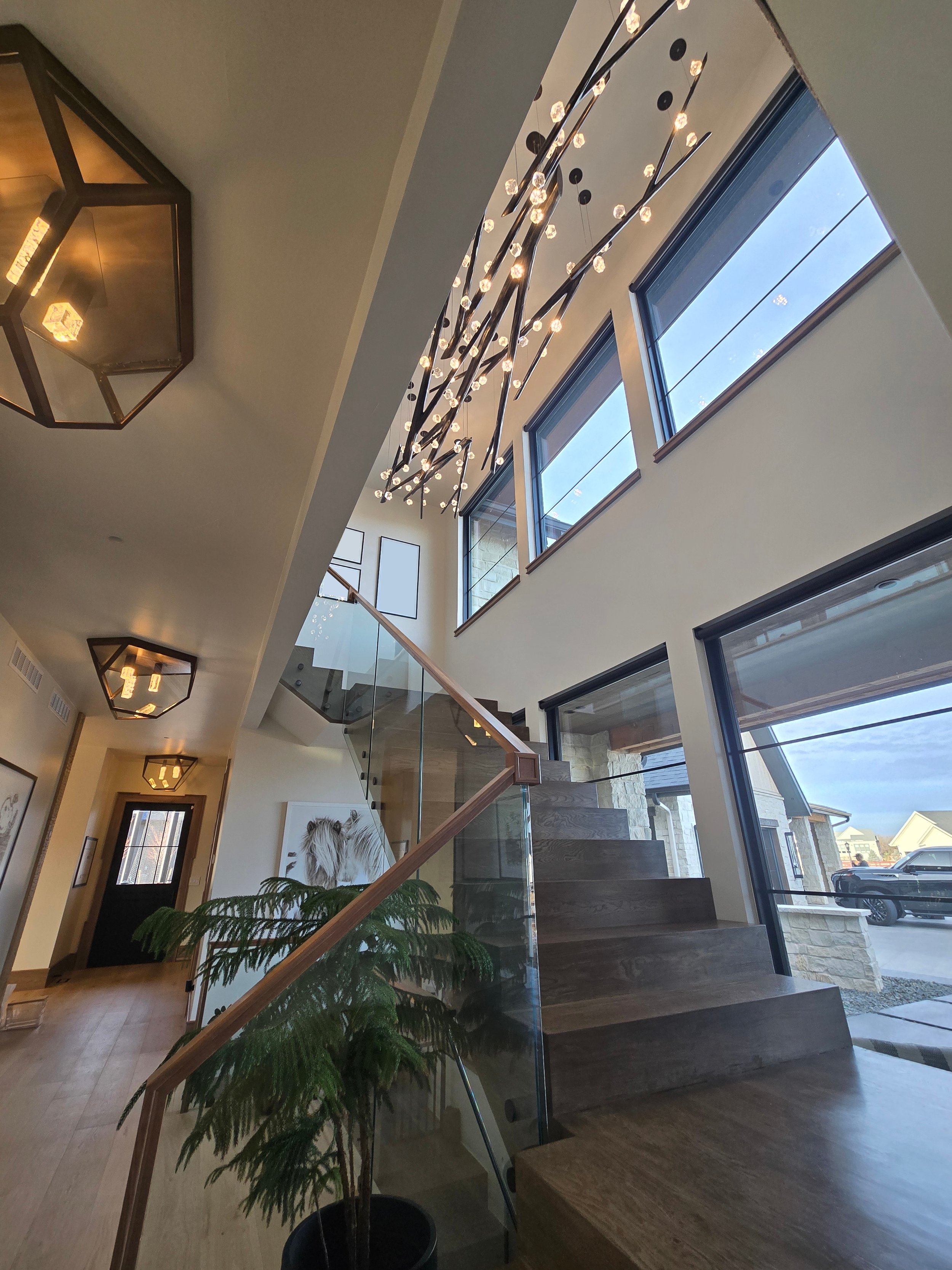 Interior view of a modern home with a staircase, large windows, and decorative ceiling lights.