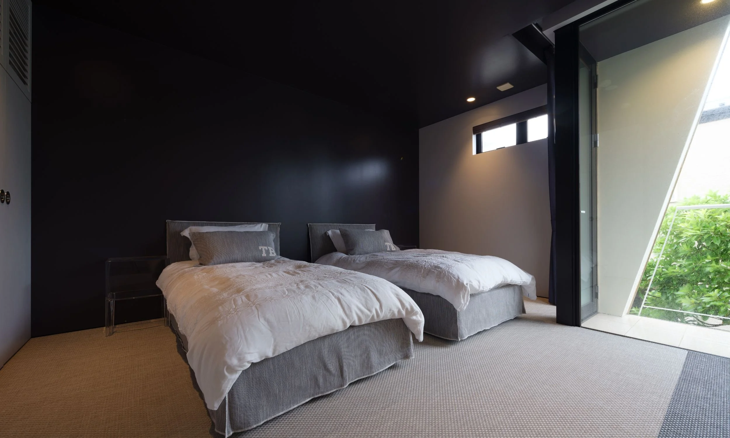 二つのベッドが置かれたモダンな洋室。窓から自然光が入り、緑の景色が見える。