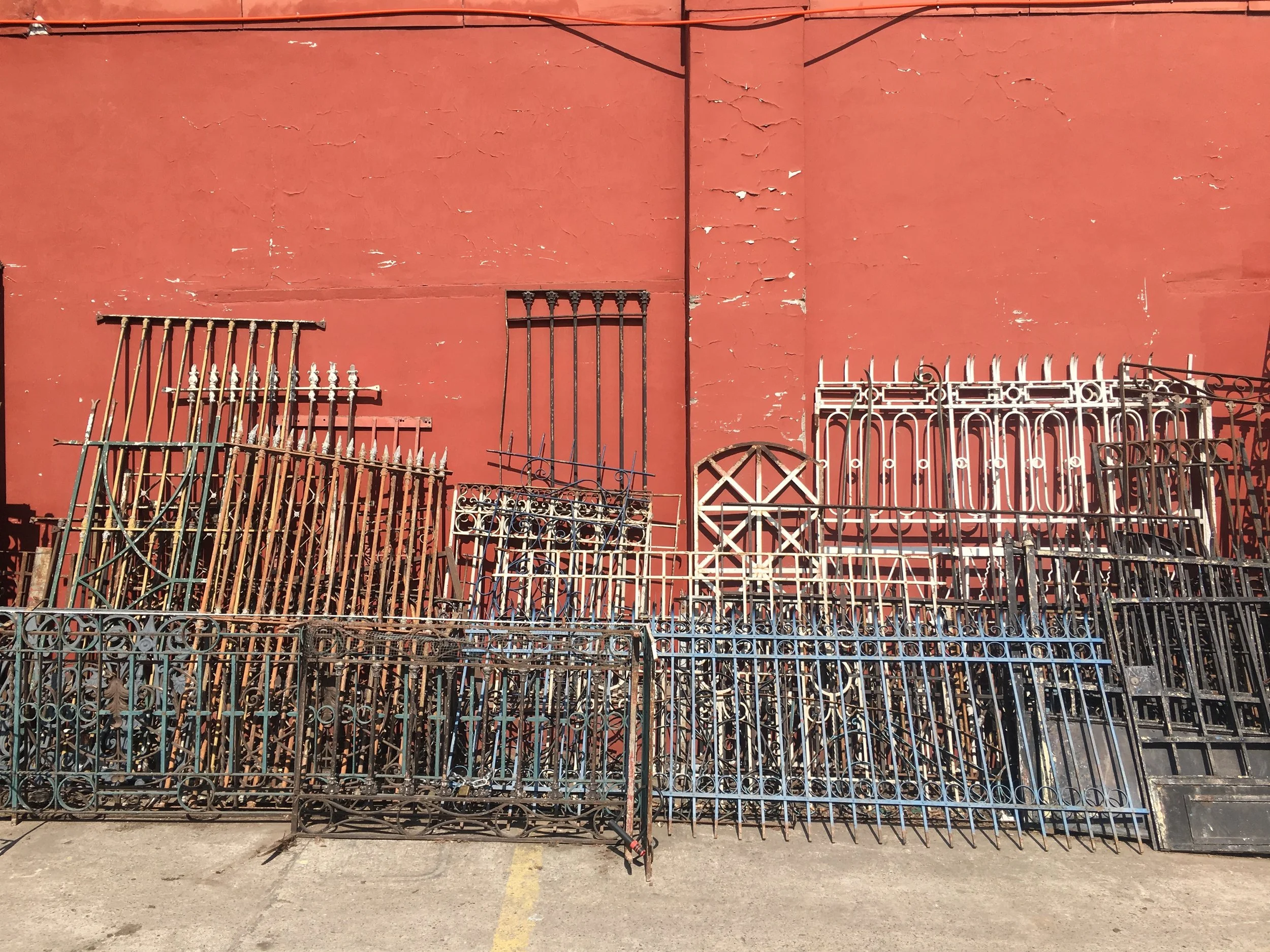 Beautiful image of a variety of old wrought iron gates different sizes, shapes and colours leaning against a vivid red/orange wall. Depicts selecting proven structures to suit your needs.