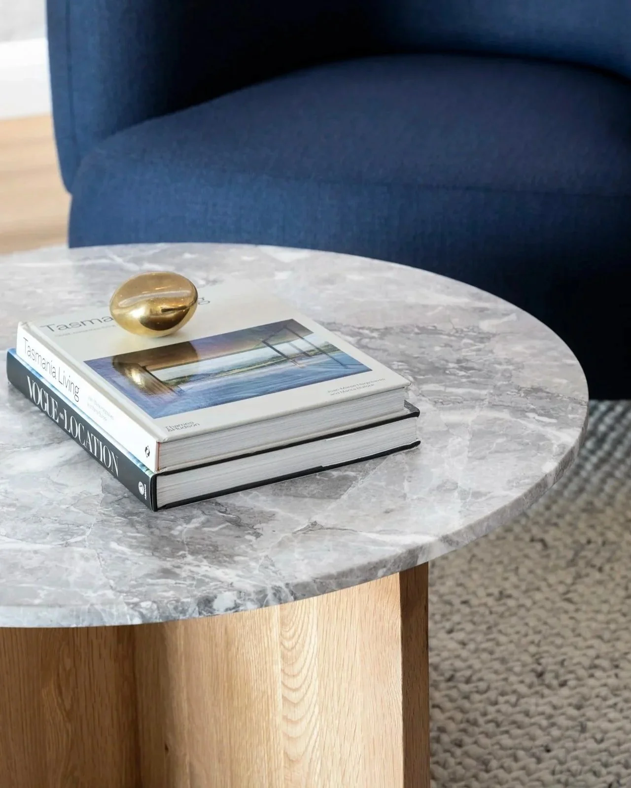 Living room with blue armchairs, a marble coffee table with books and a decorative object, a side table with marble top, and a patterned rug.