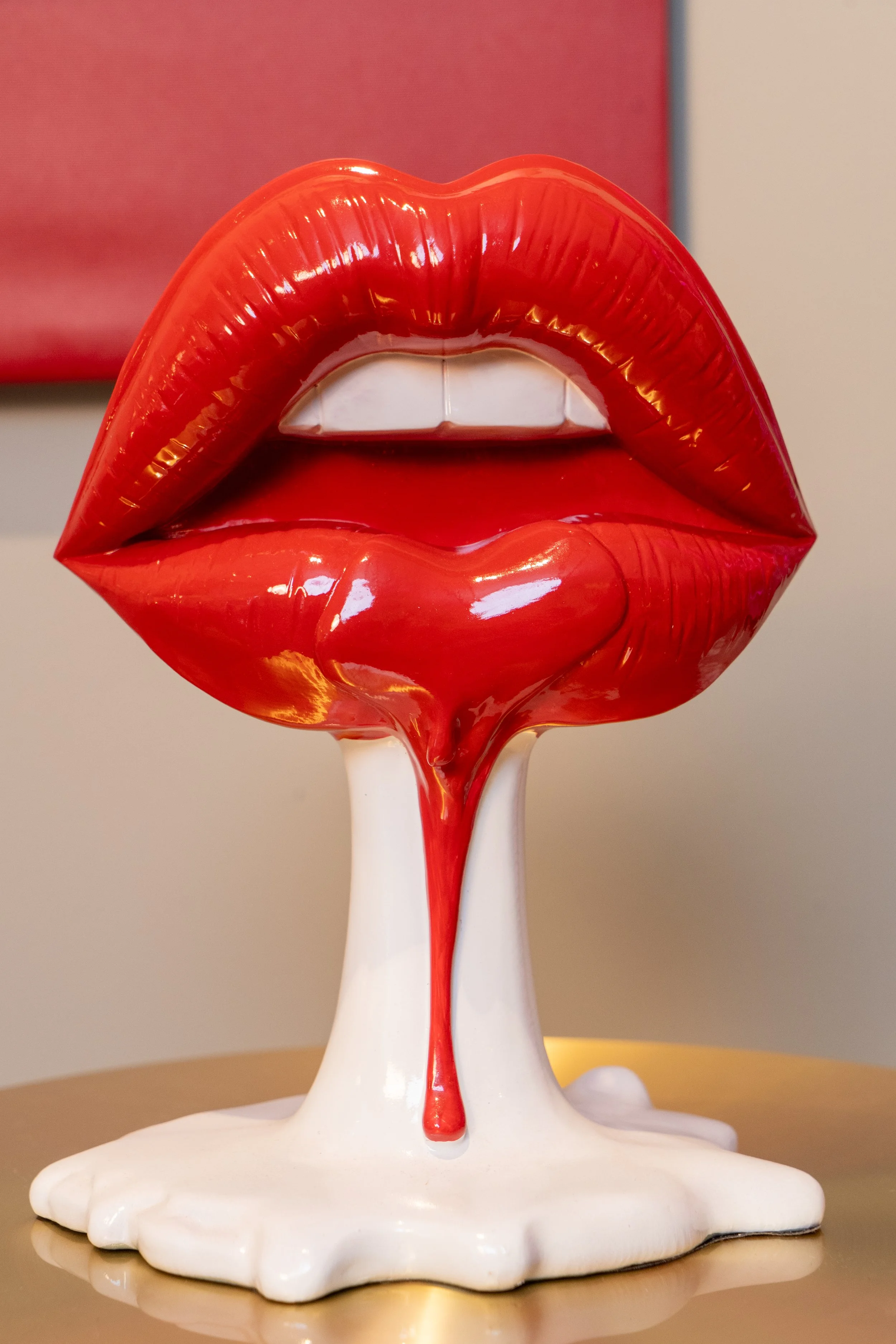 A sculpture of red lips with a tongue, with red liquid dripping down, set on a white base.