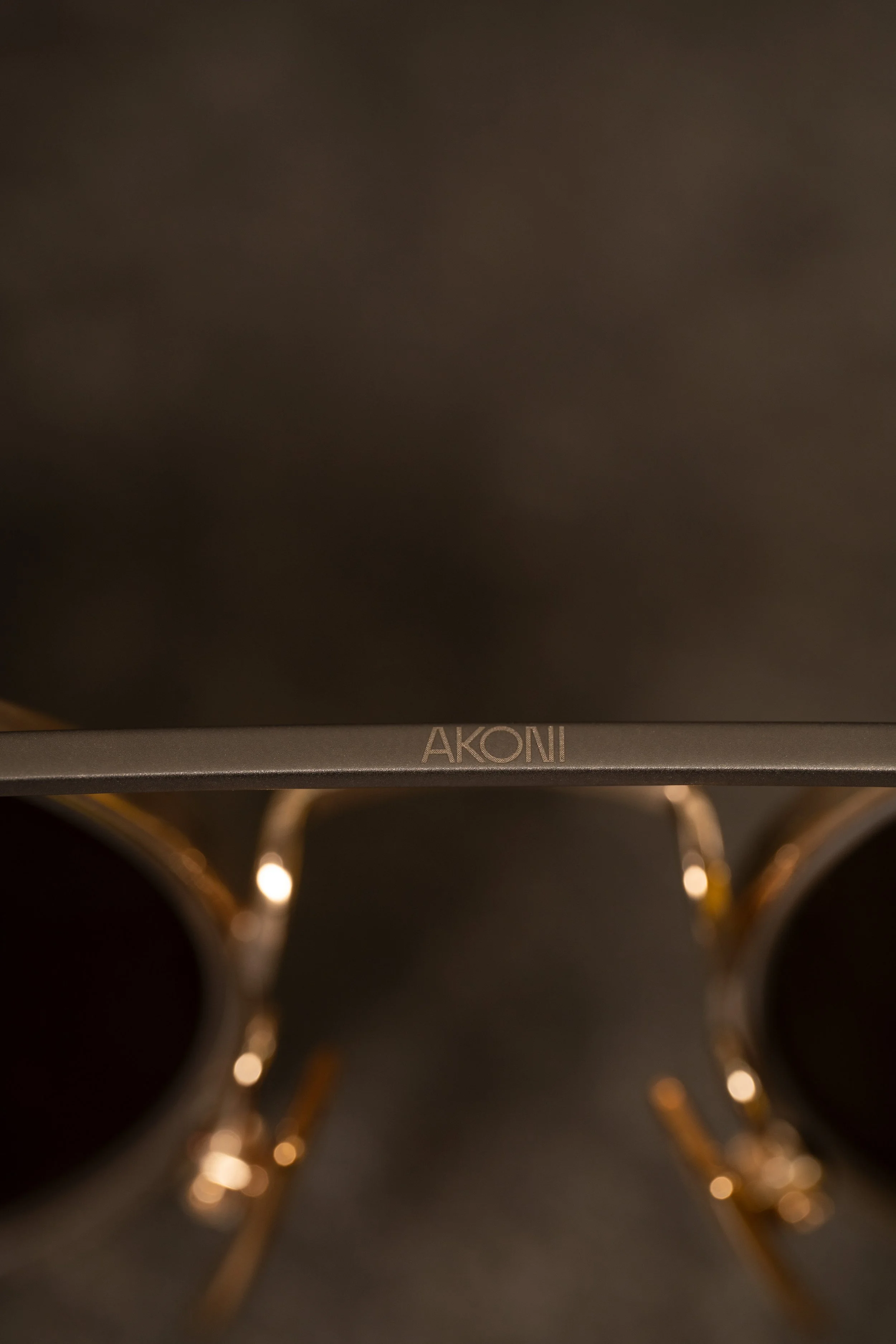 Close-up of an Akoni branded electronic device with a pair of black and gold sunglasses placed below it.