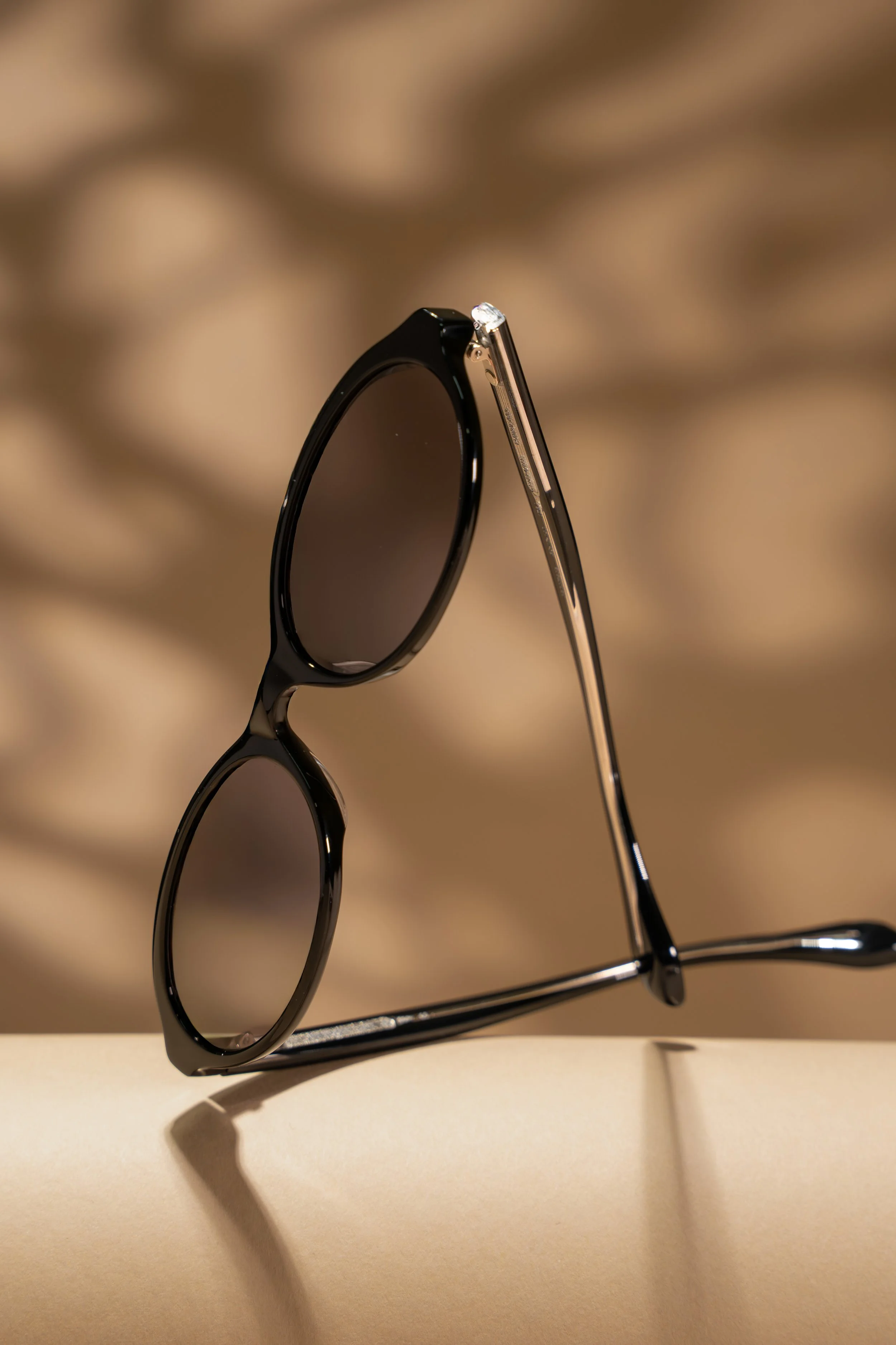 A pair of black sunglasses balanced on a surface with a warm, blurry background.