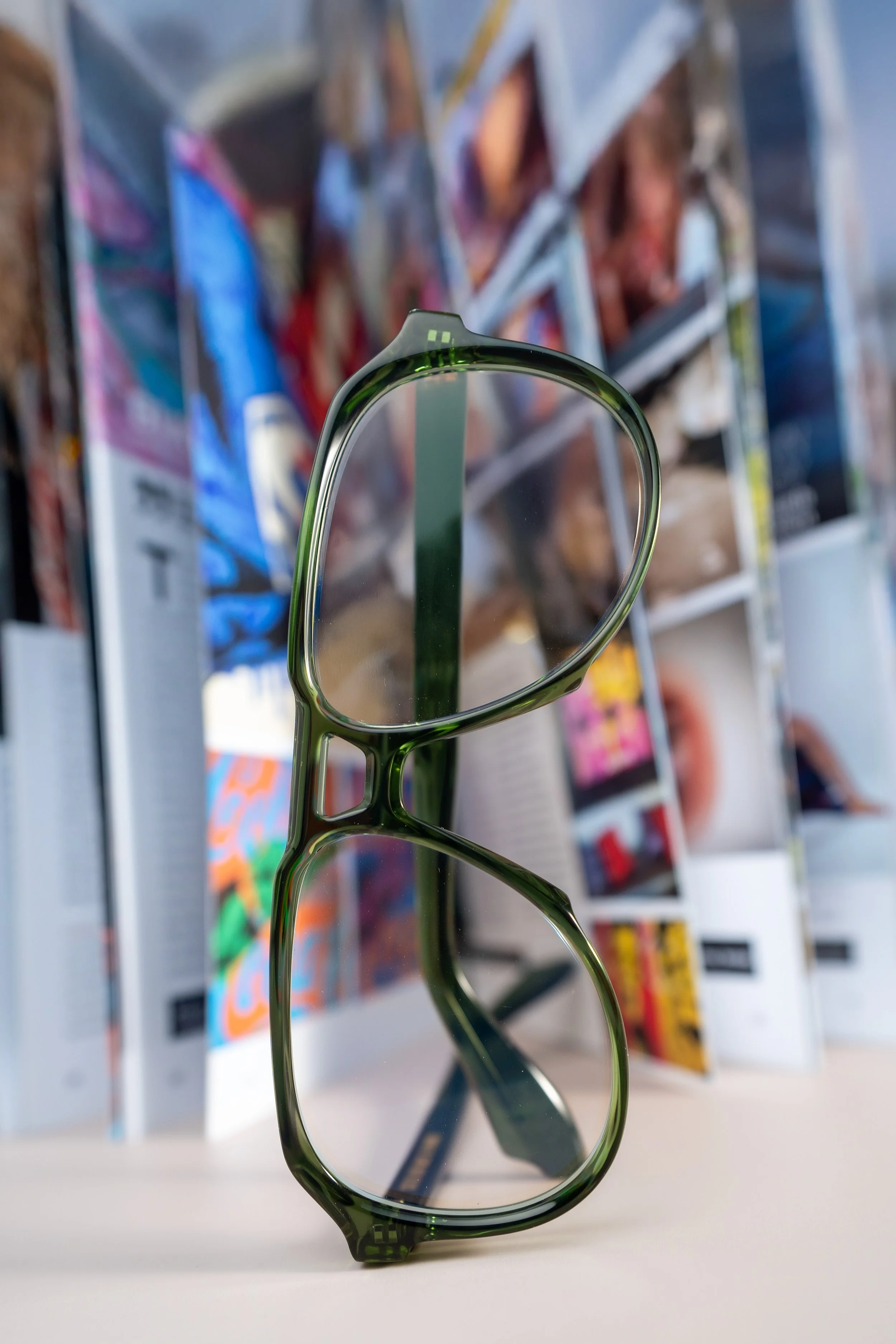 A pair of green-rimmed eyeglasses on a white surface with colorful magazines or comic books in the background.