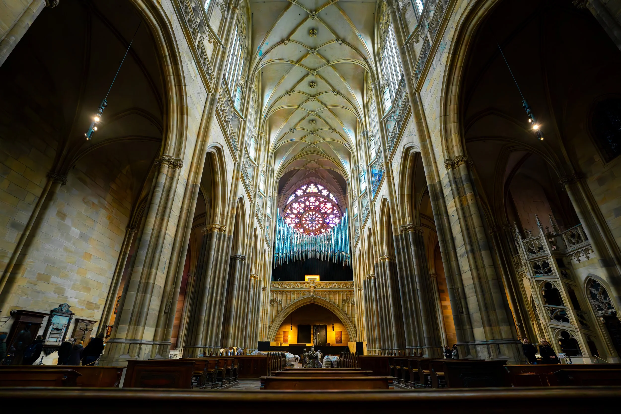 Interior of a Gothic cathedral with high vaulted ceilings, large stained glass window at the end, and stone pillars lining the nave.