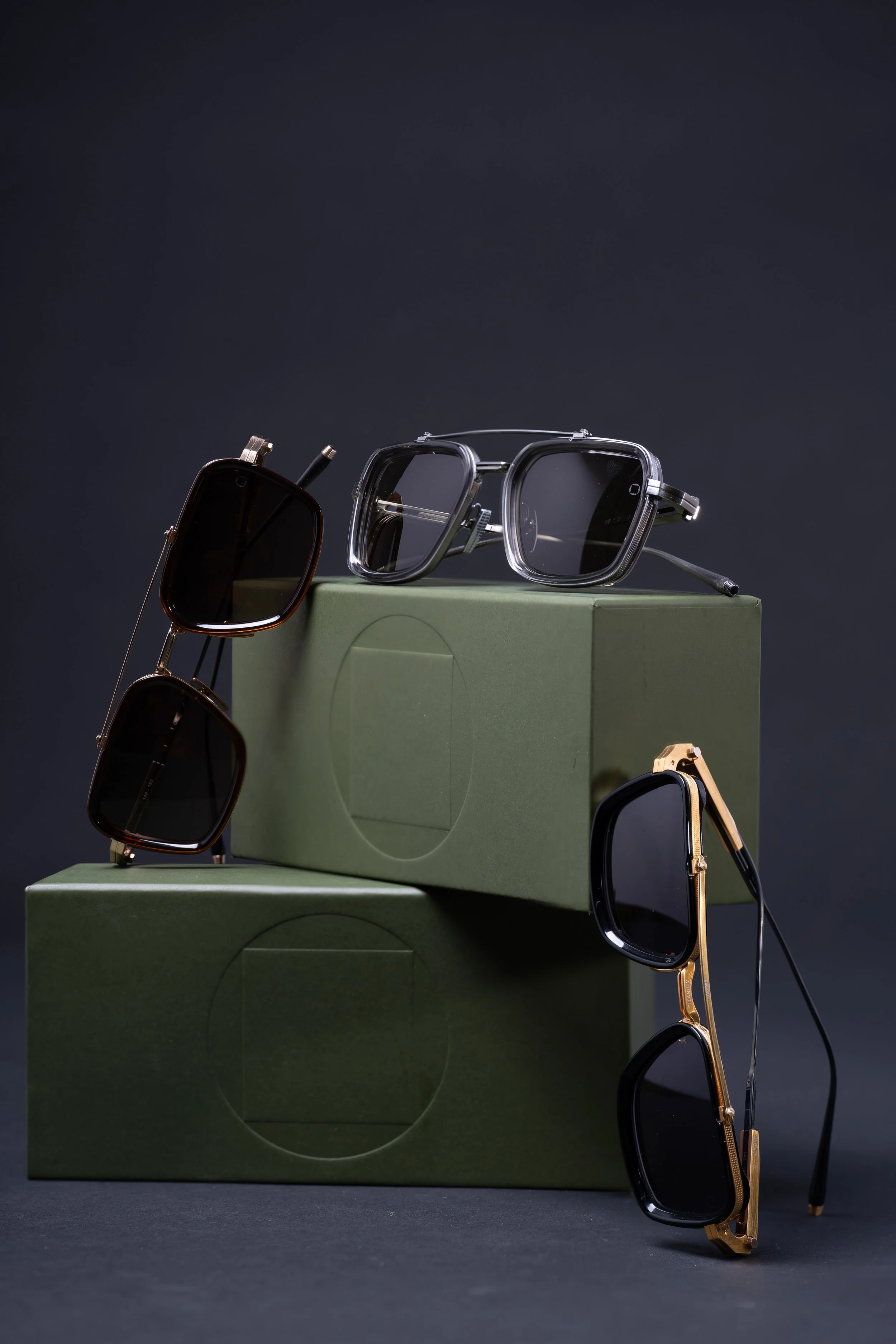 Three pairs of sunglasses placed on two green boxes against a dark background.