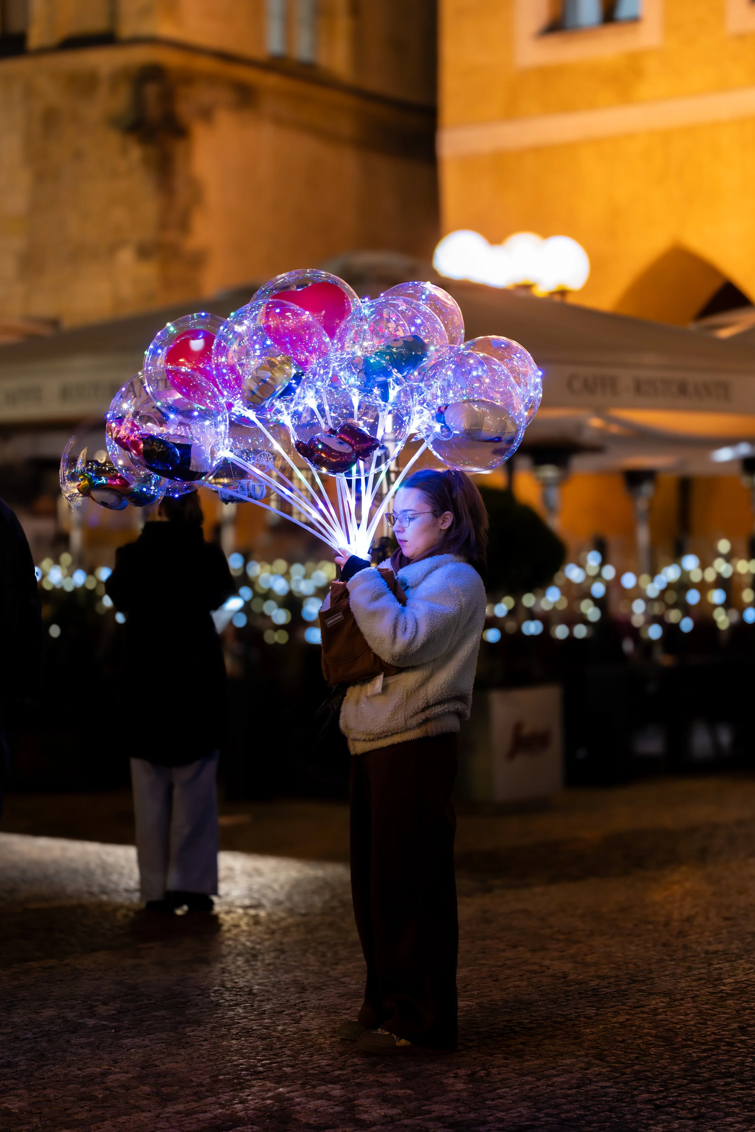 A woman holding illuminated balloon lights at night in an outdoor setting.