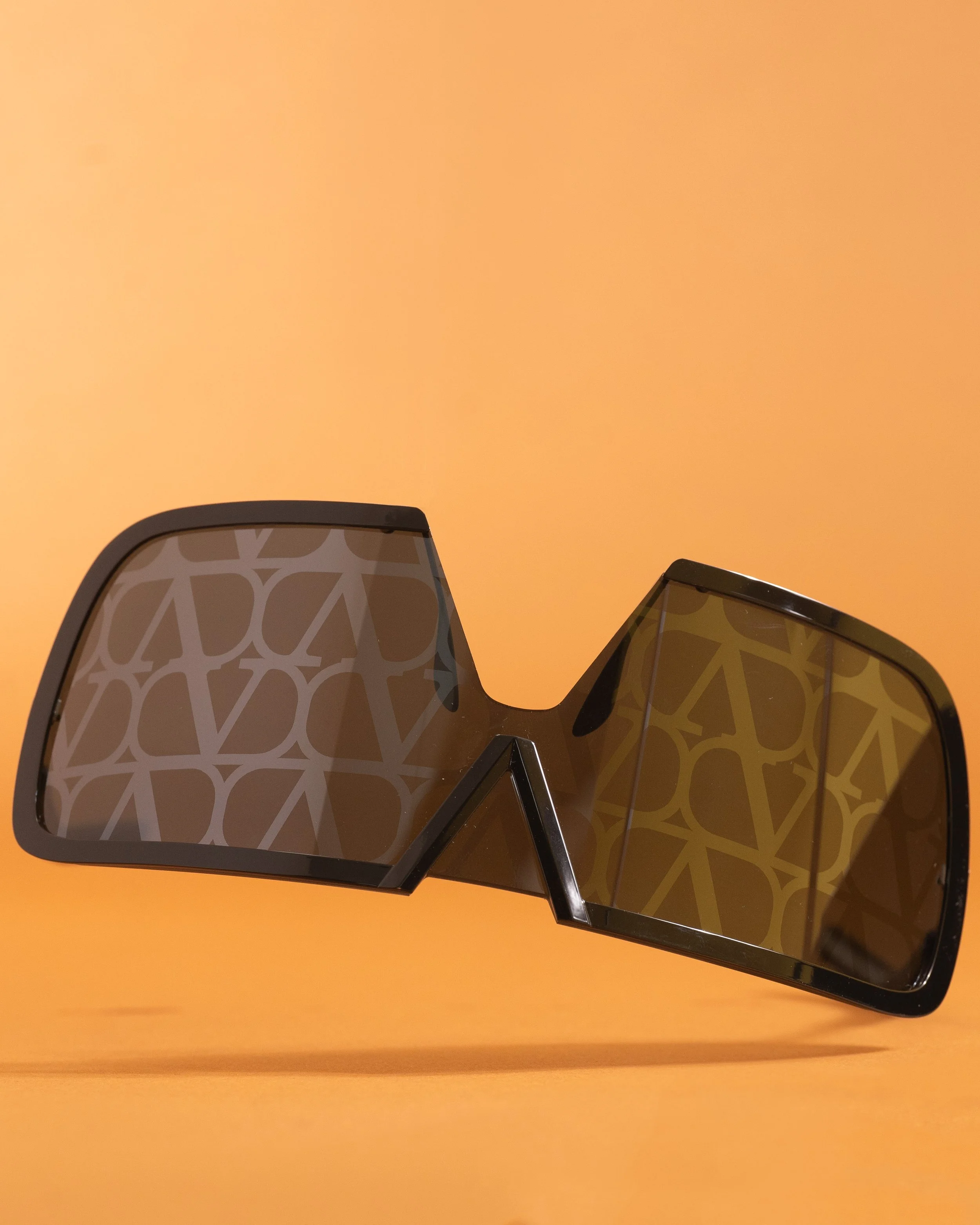 Fashion sunglasses with dark tinted lenses and geometric pattern, set against an orange background.