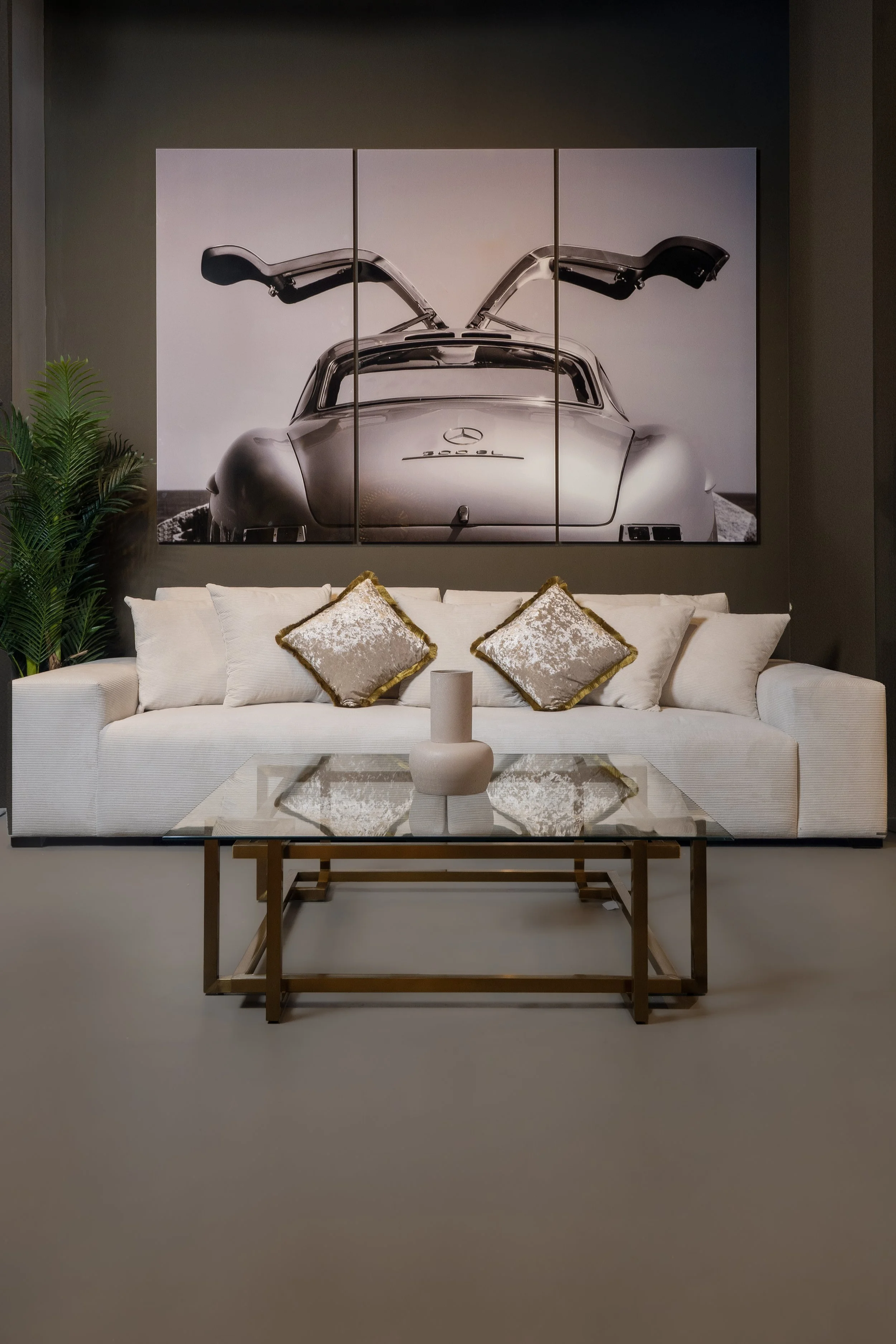 Living room with a white sofa, decorative pillows, a glass coffee table, a vase, and a large artwork of a vintage Mercedes-Benz car with gull-wing doors.