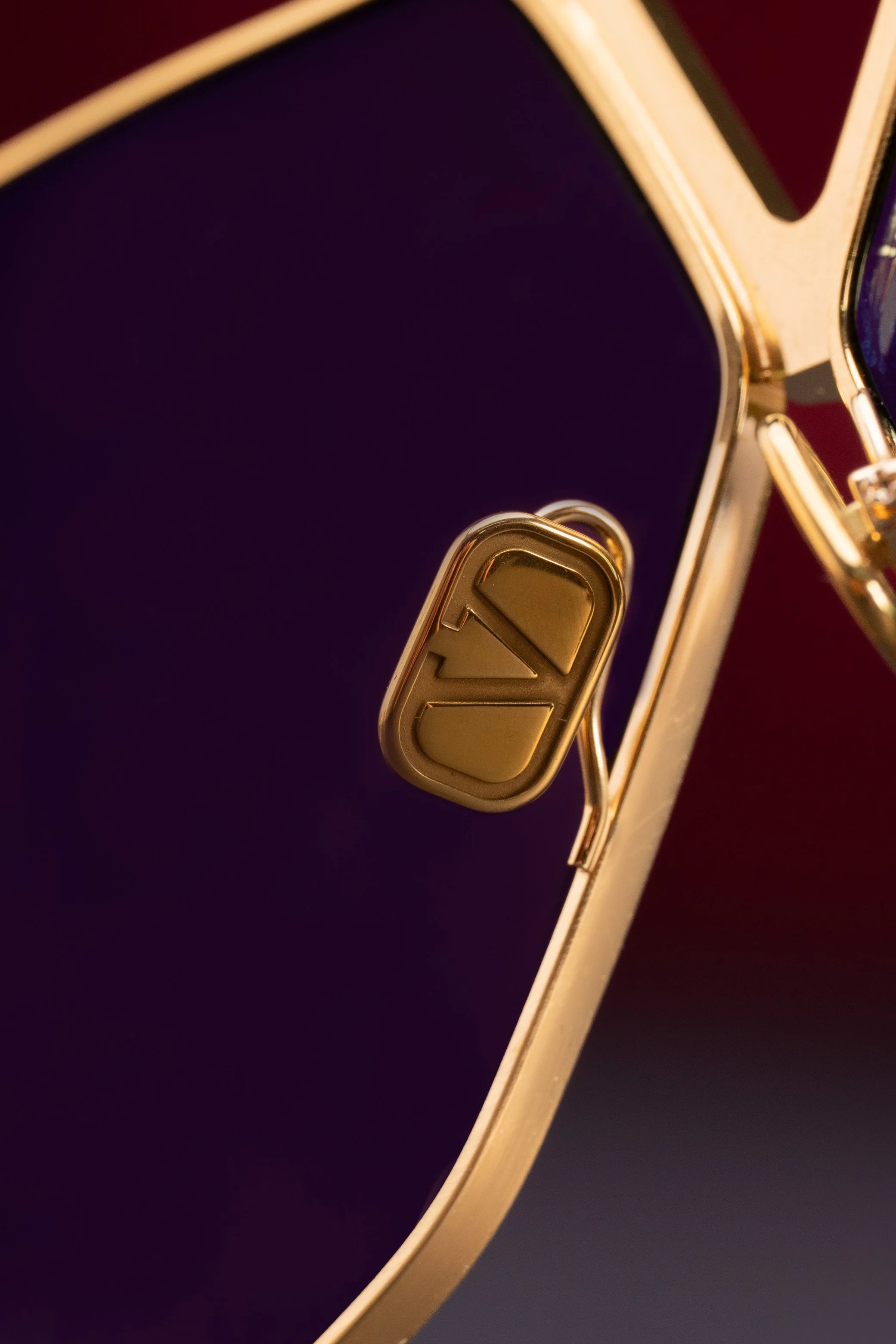 Close-up of a gold-colored sunglasses with the left hinge and temple visible, featuring the 'LV' logo emblem on the hinge.