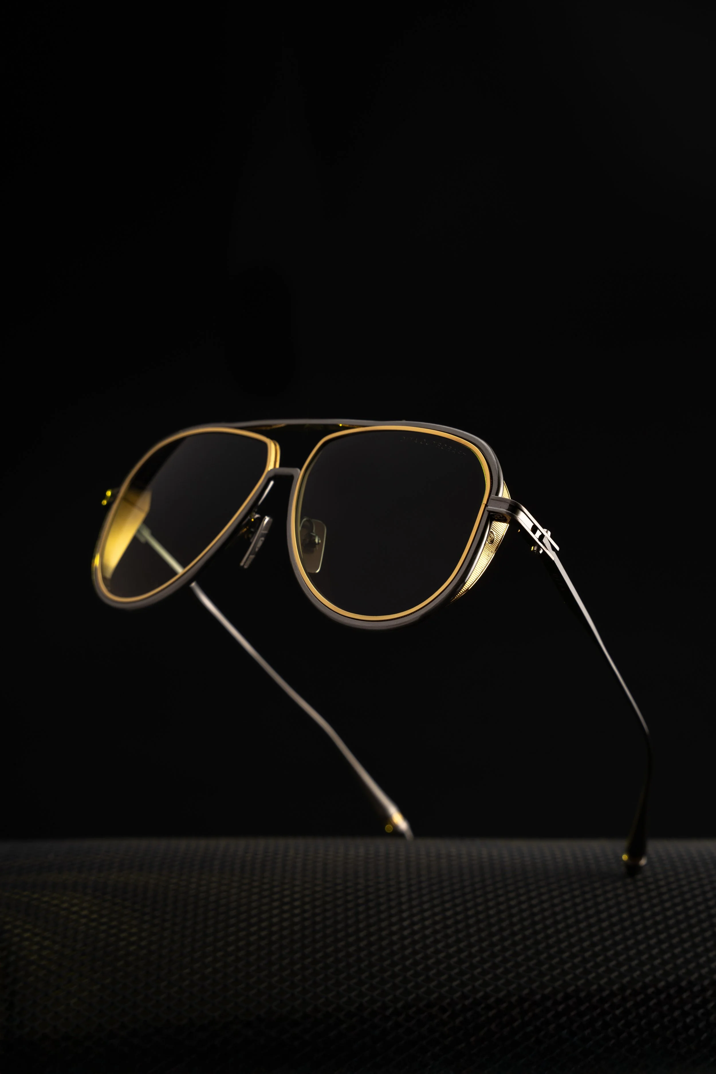 A pair of black sunglasses with gold accents on the frame, set against a black background.