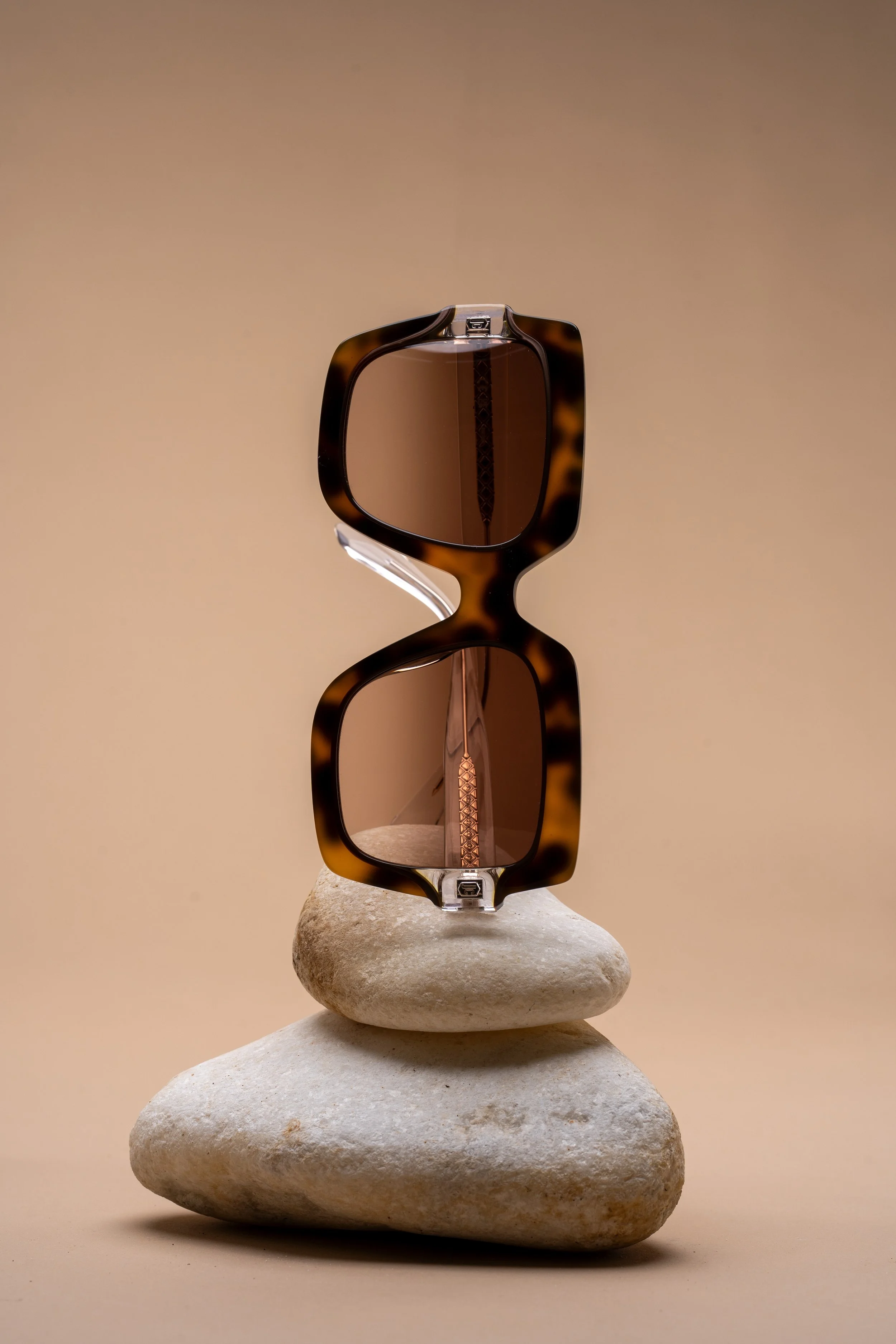 A pair of tortoiseshell sunglasses balanced on two stacked stones against a beige background.