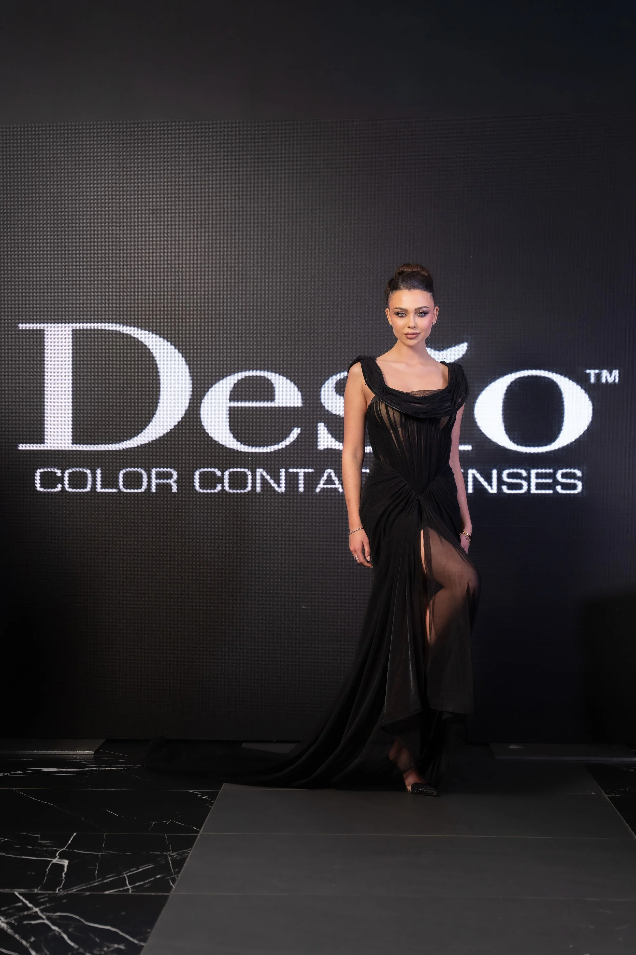 A woman in a black evening gown walking on a runway during a fashion show.